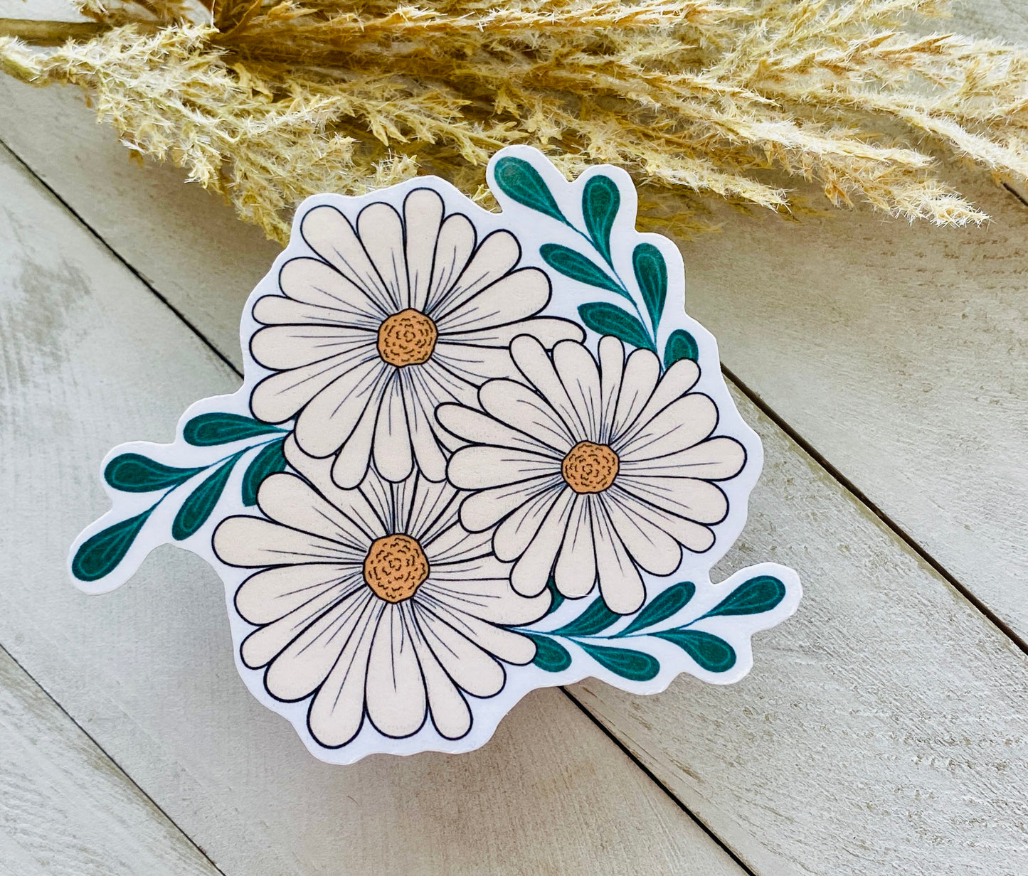 A sticker depicting three daisies against a wood background