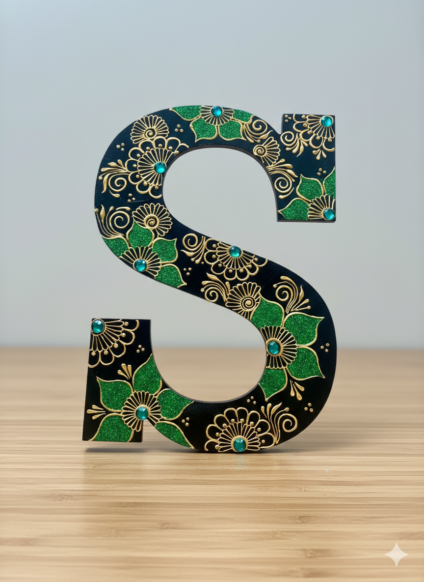 Decorative letter 'S' with green and gold floral patterns on a wooden surface.