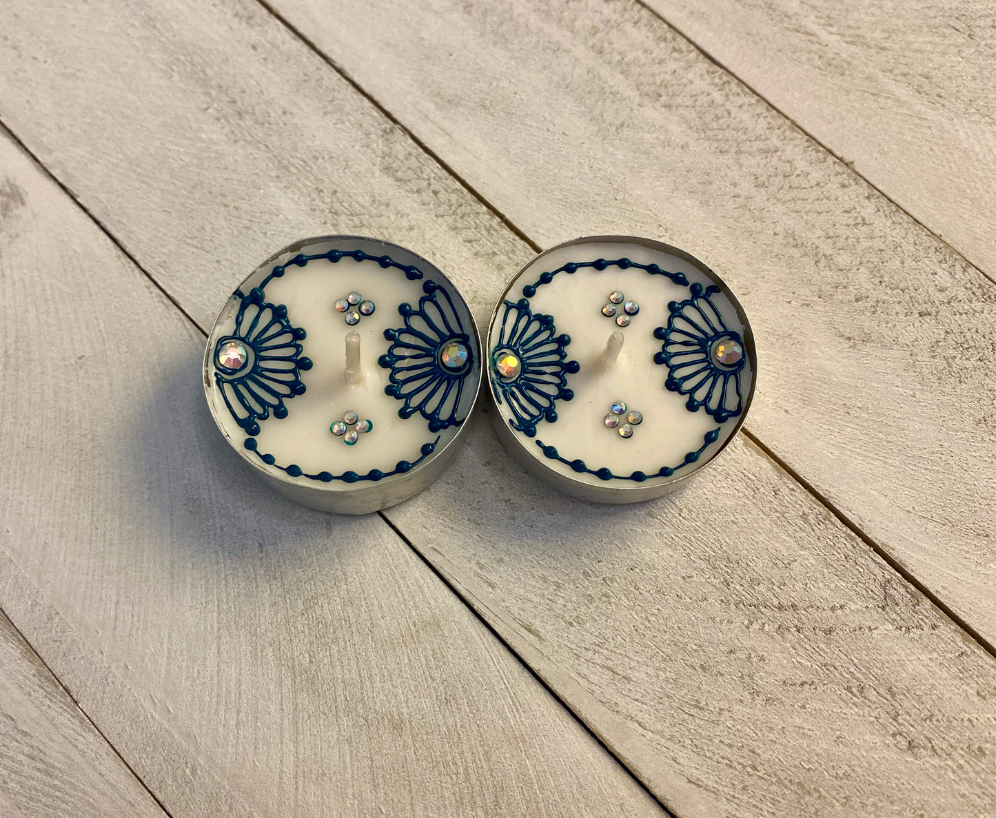 Two floral tea lights painted in a blue color with gemstones on a wood background 