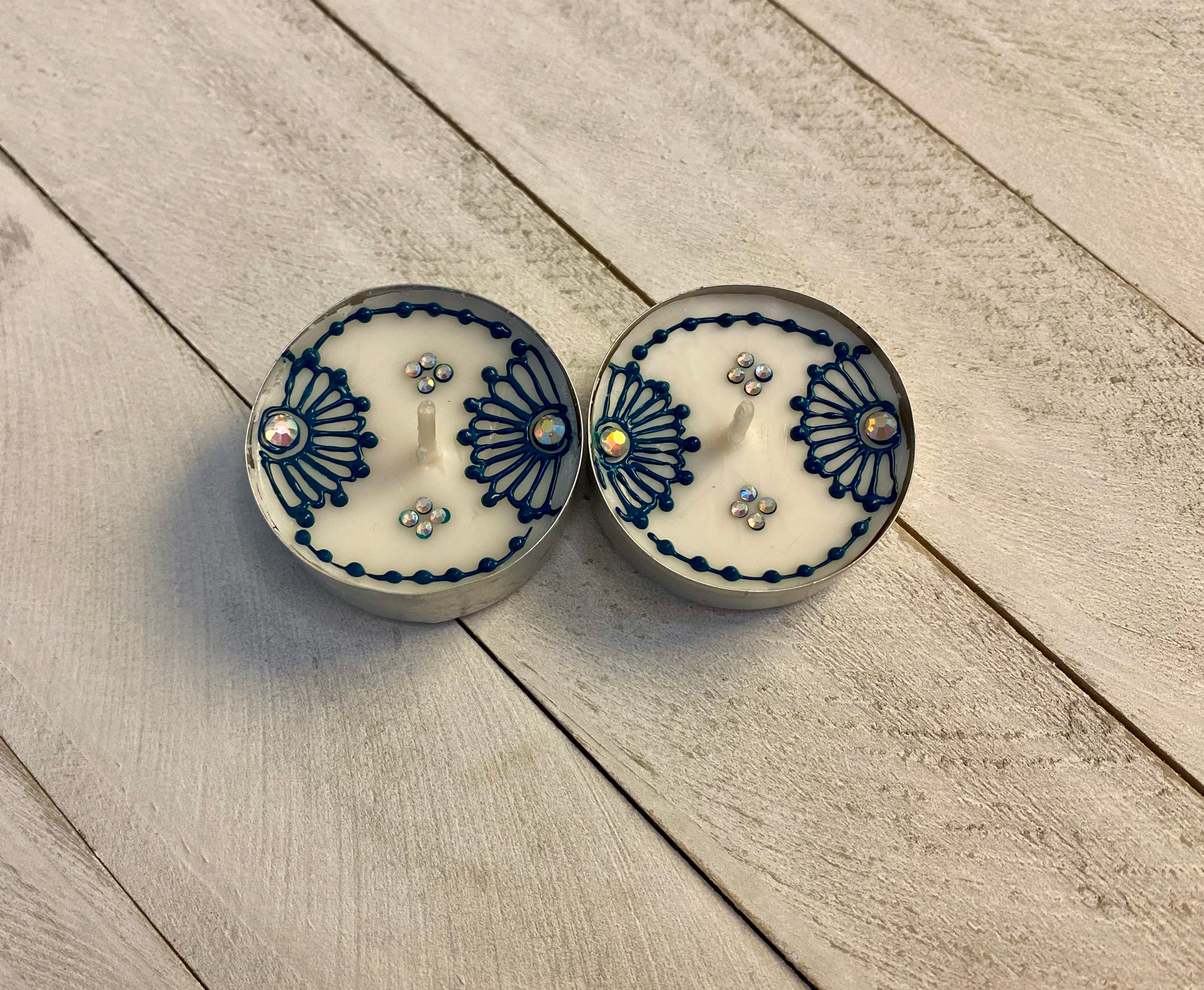 Two floral tea lights painted in a blue color with gemstones on a wood background 