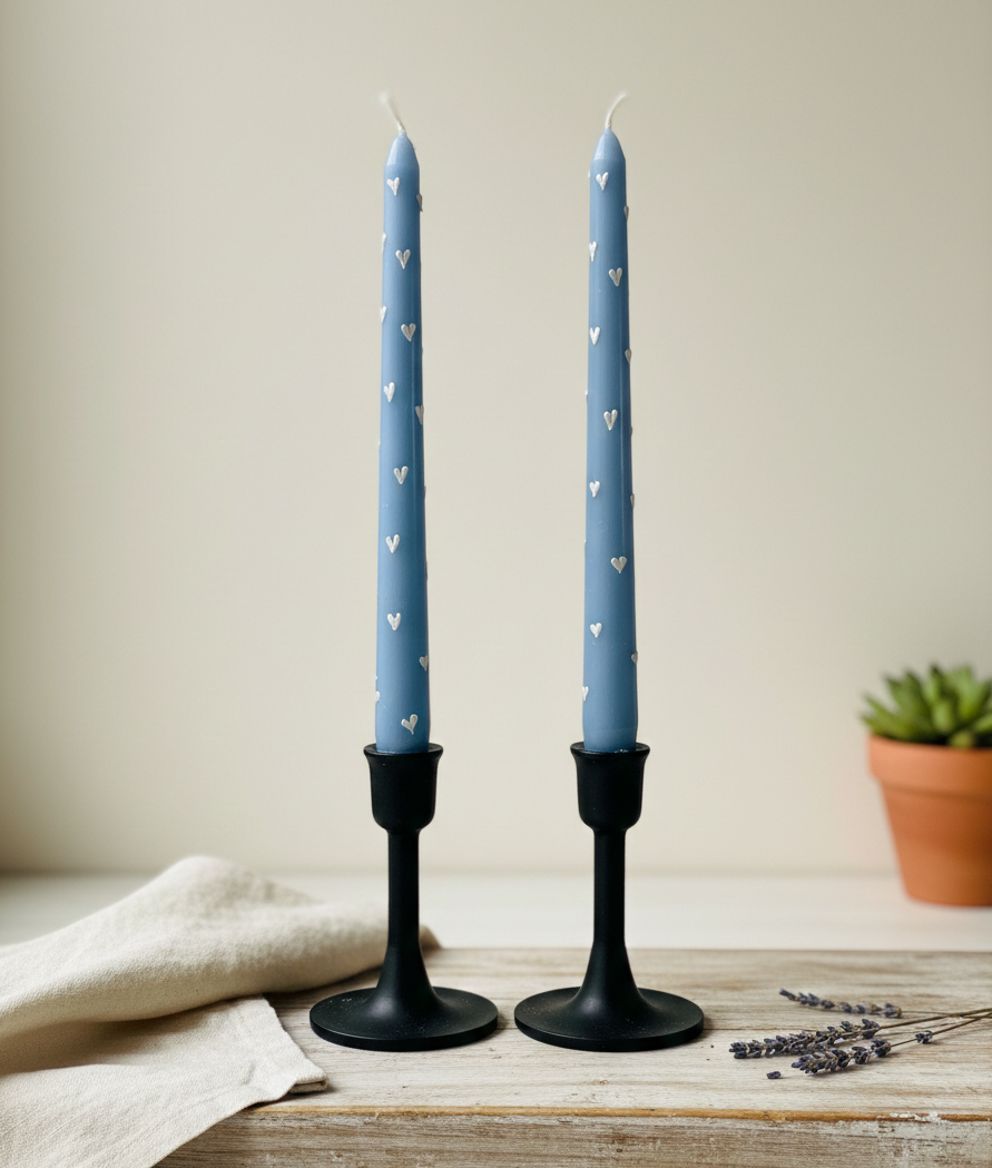 Two blue candles with heart patterns on black candlesticks on a wooden surface.