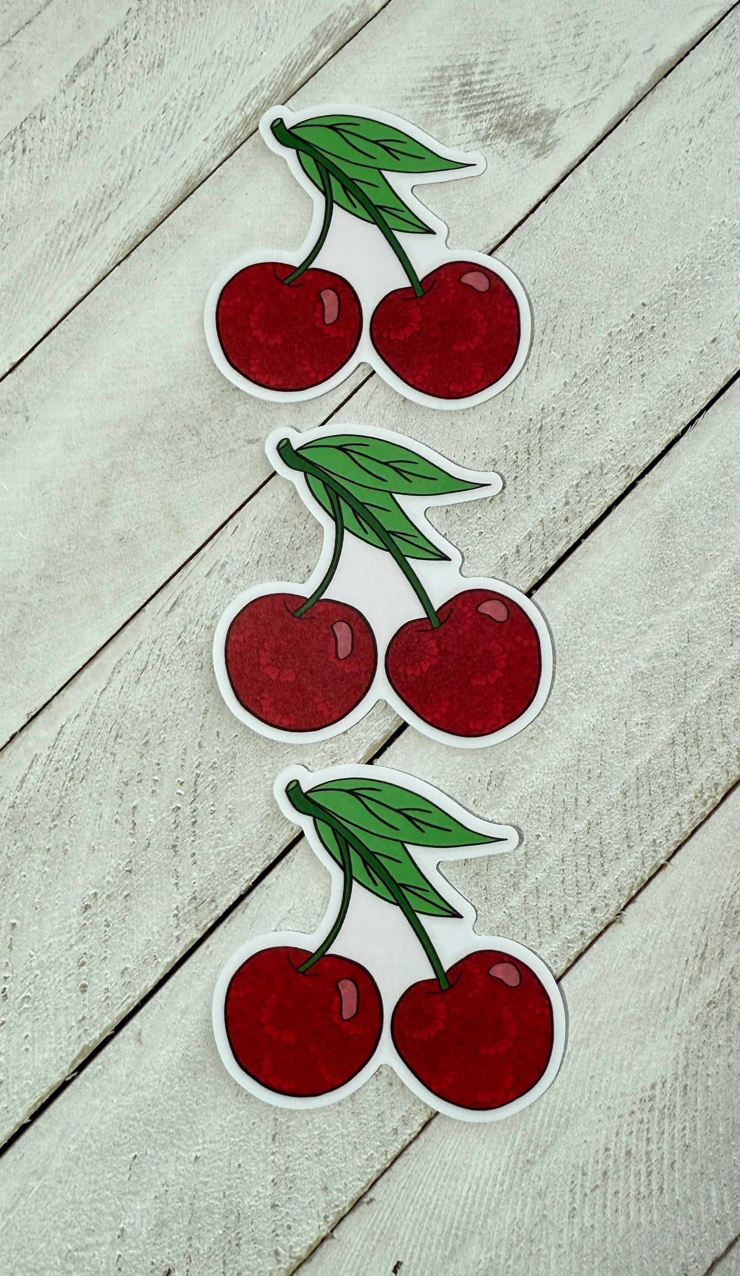 Three cherries stickers in a row on a wood surface 