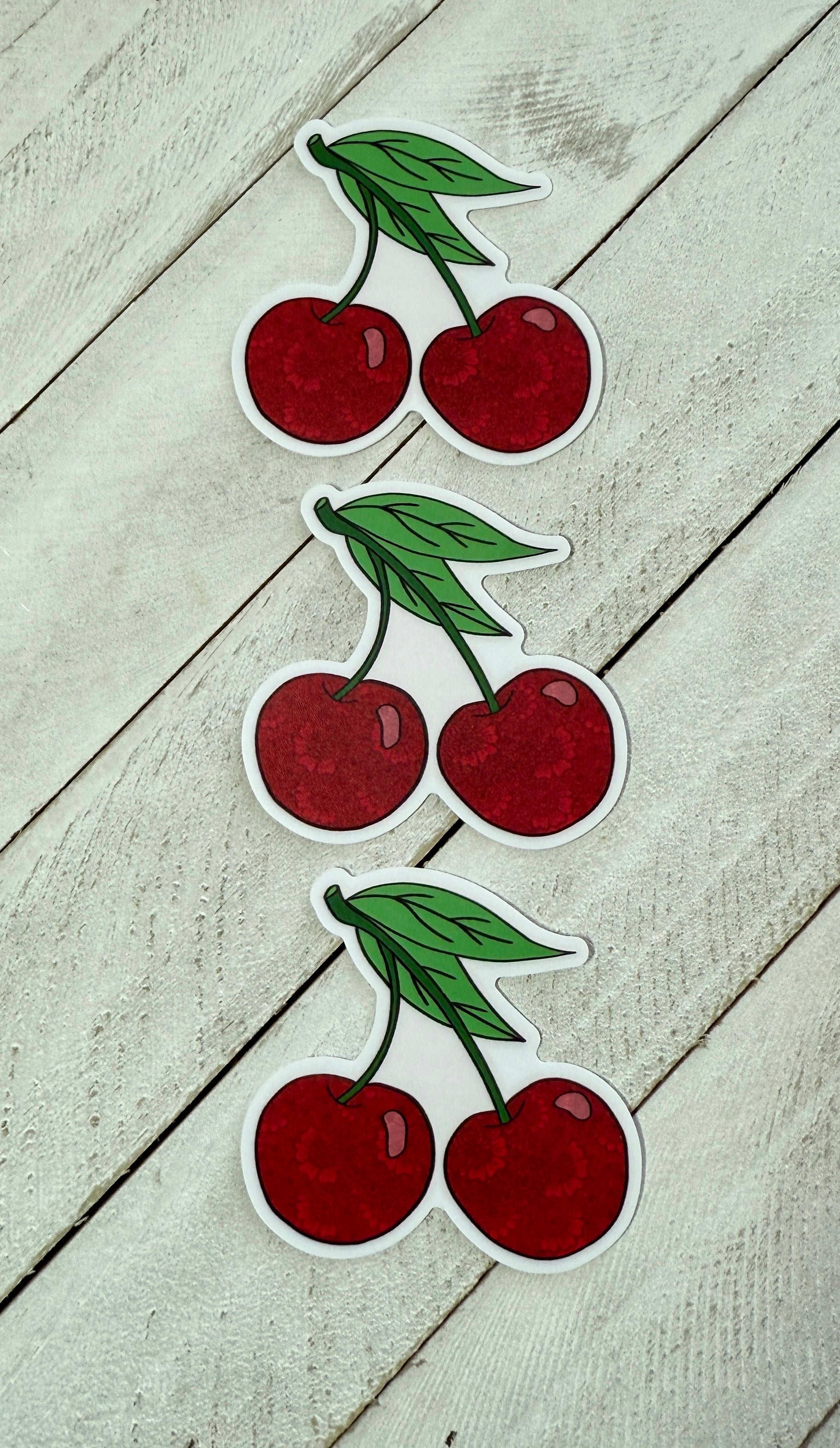 Three cherries stickers in a row on a wood surface 