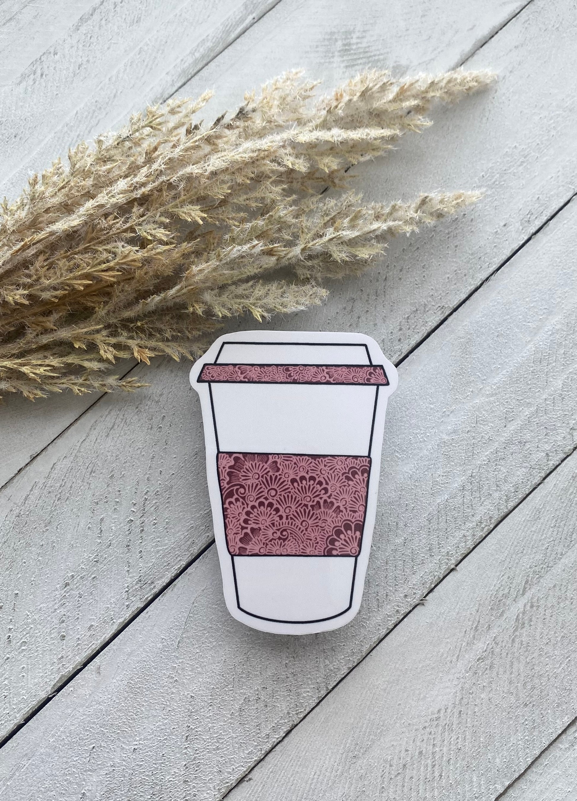 Coffee Cup Sticker with pink henna design on a wood background with a dried plant on the side 