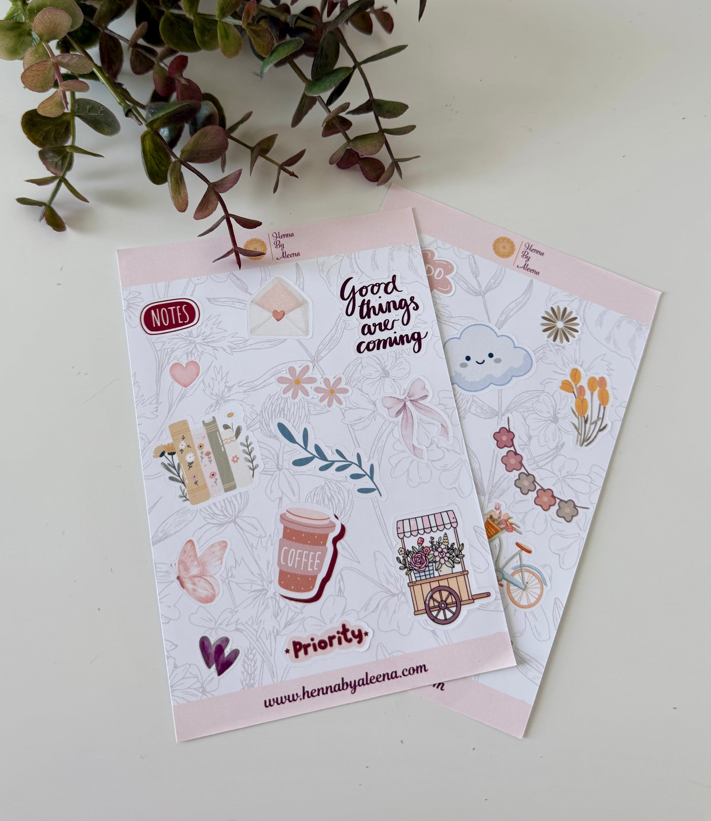 Two sticker sheets with illustrations and text on a light background with greenery.
