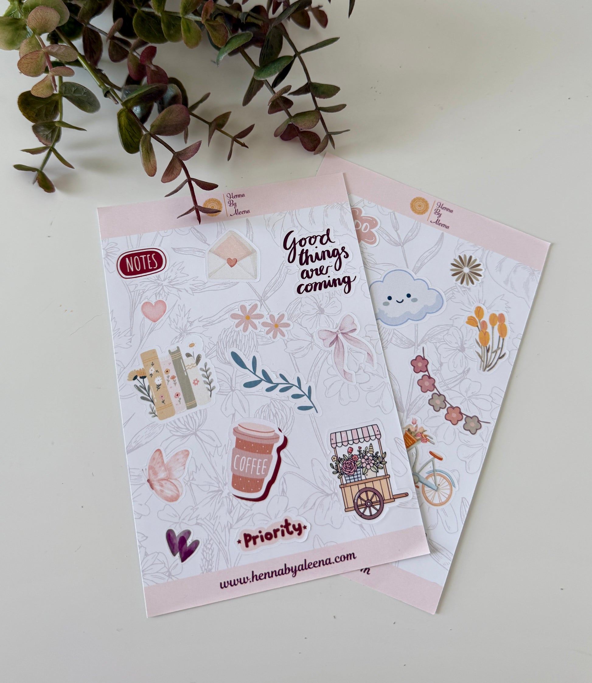 Two sticker sheets with illustrations and text on a light background with greenery.