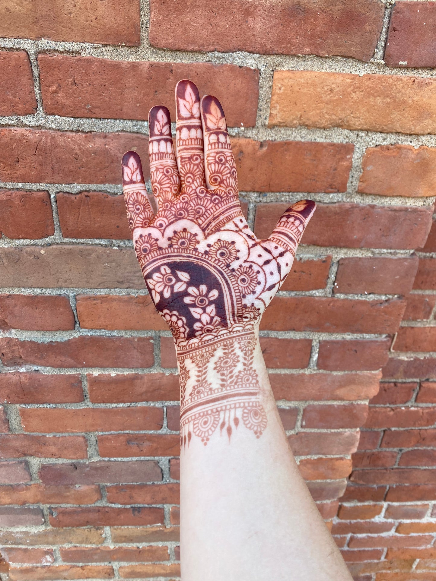 A hand with a dark red/brown henna stain against the bricks of a building 