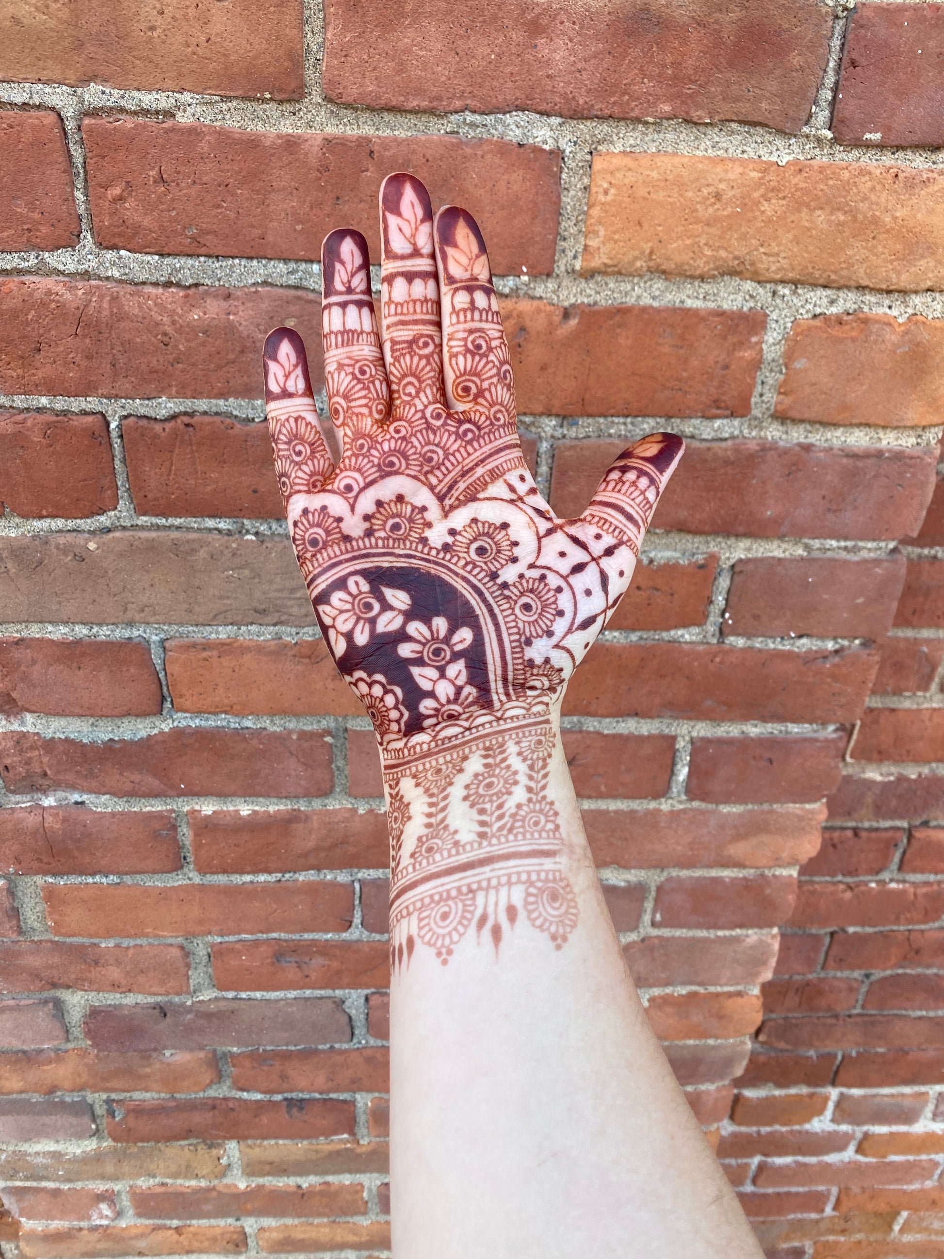 A hand with a dark red/brown henna stain against the bricks of a building 