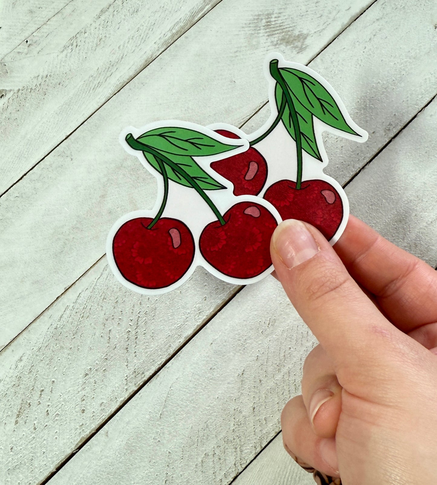 Hand holding two cherry stickers on a wood background 