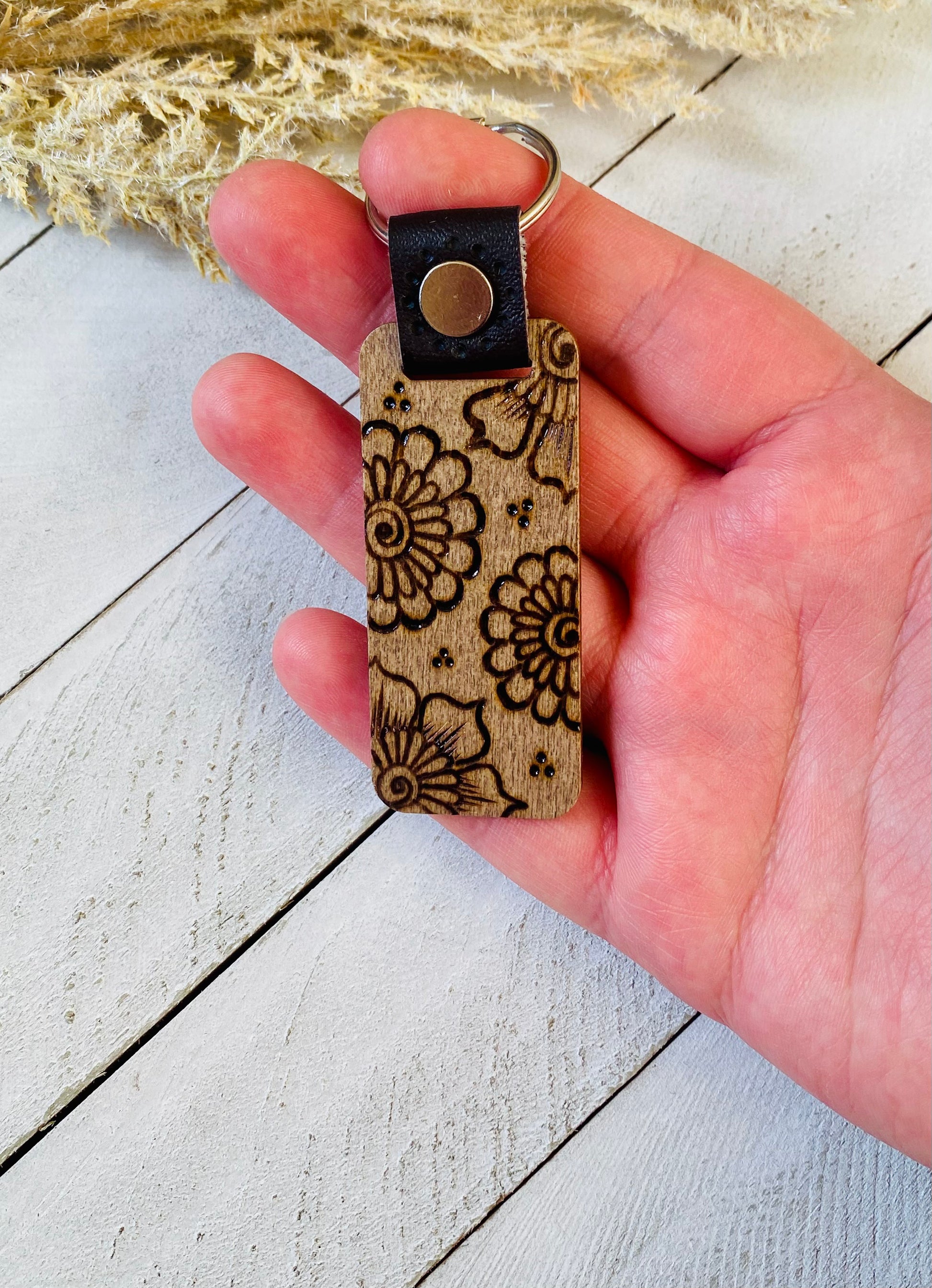 Hand holding keychain with a floral henna inspired design over a wood background 