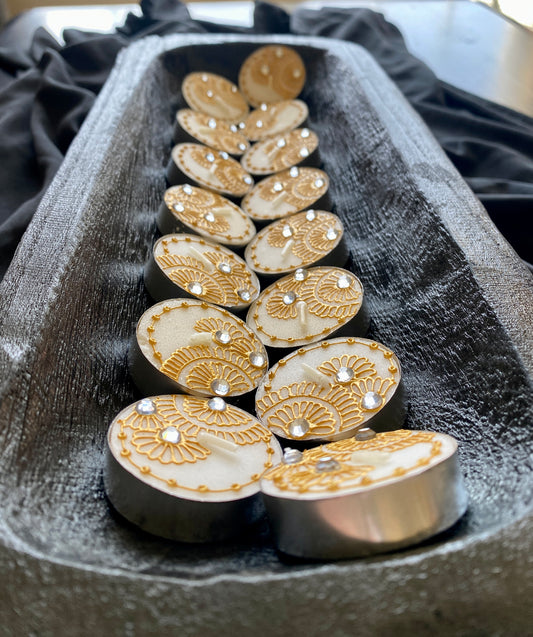 A row of hand-painted tea lights with gold acrylic paint and rhinestones, displayed on a textured surface.