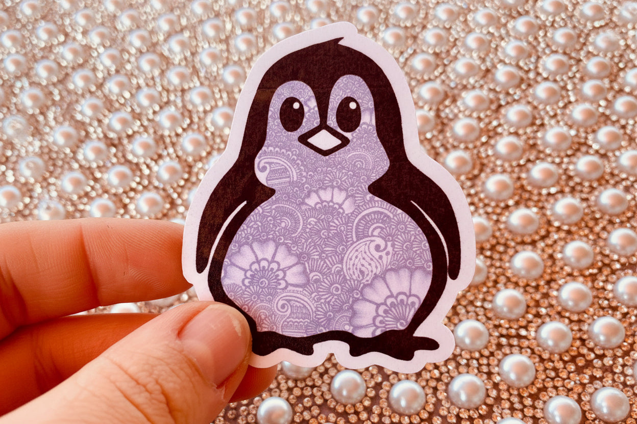 A hand holding a cute penguin sticker with detailed henna designs against a sparkle background 