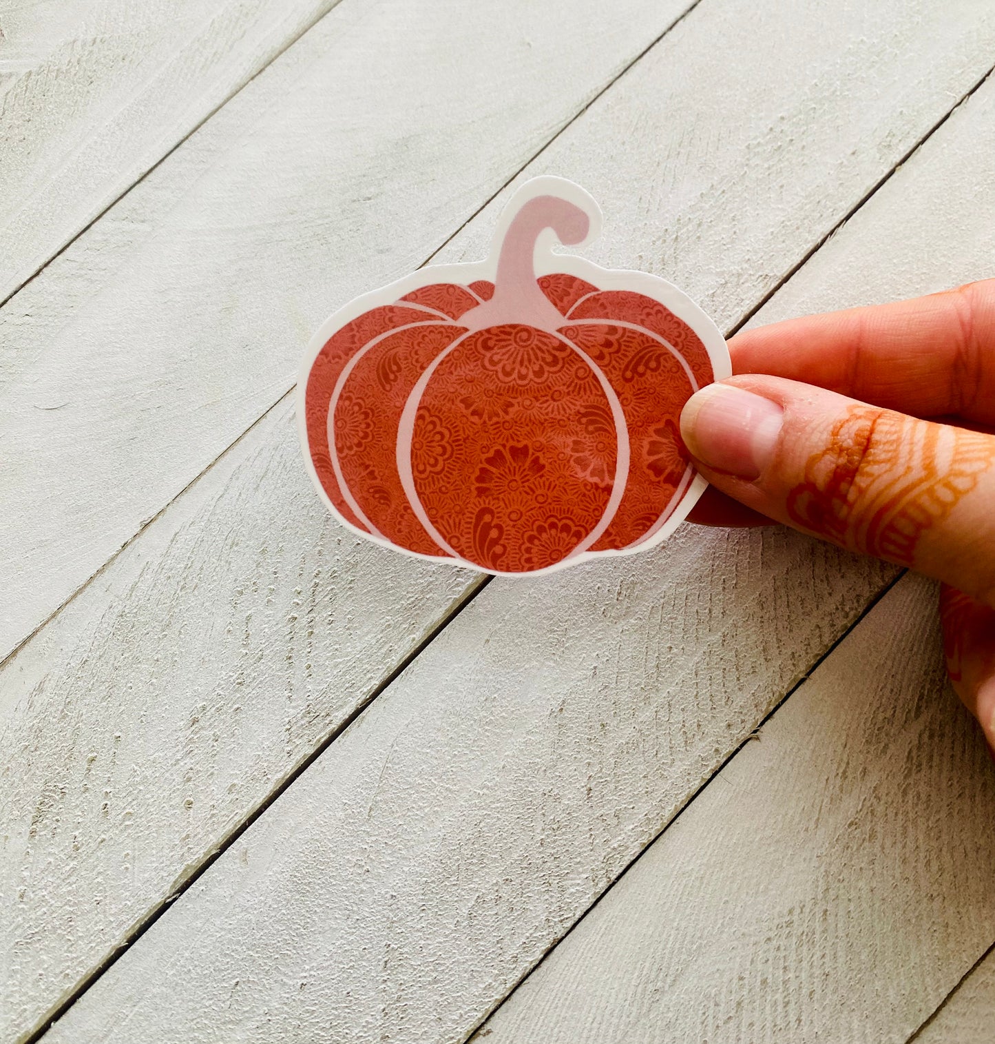 A hand holding a henna pumpkin sticker over a wood background