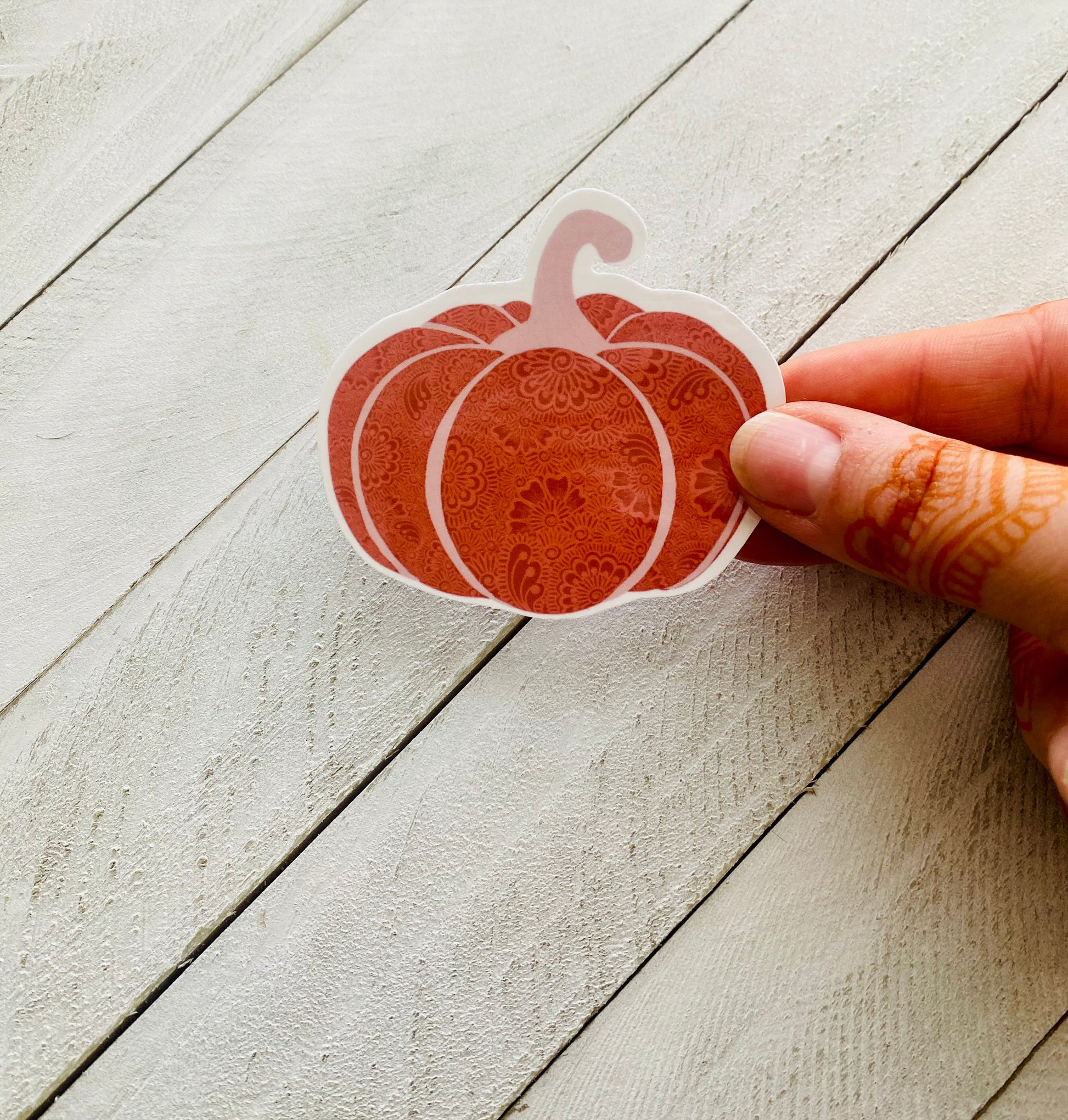 A hand holding a henna pumpkin sticker over a wood background