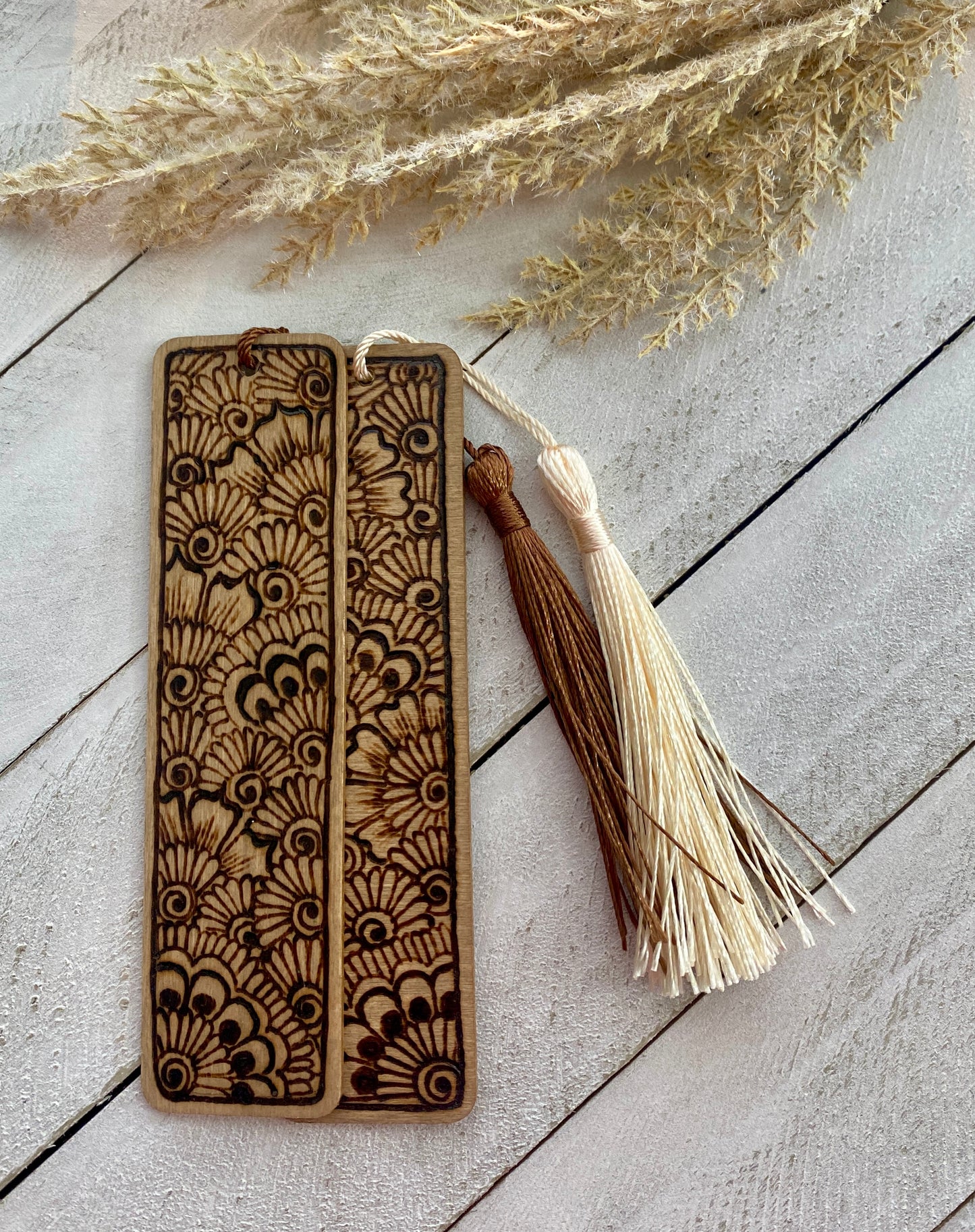 Two full henna bookmarks with cream and brown tassels on a wood surface 
