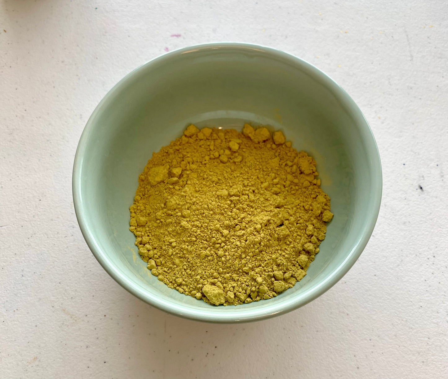 Henna powder in a green bowl, sitting on a white table 