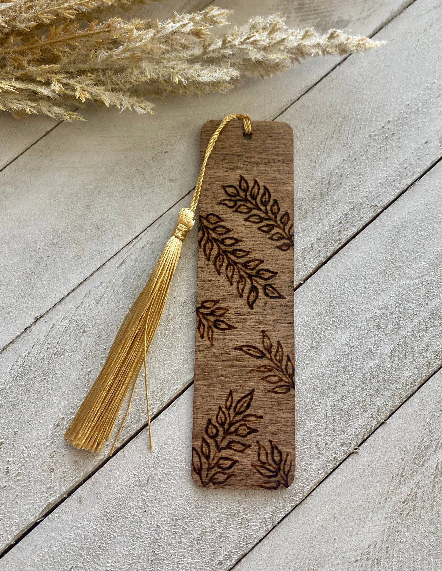 Bookmark depicting henna vines design with a gold tassel on a wood background 