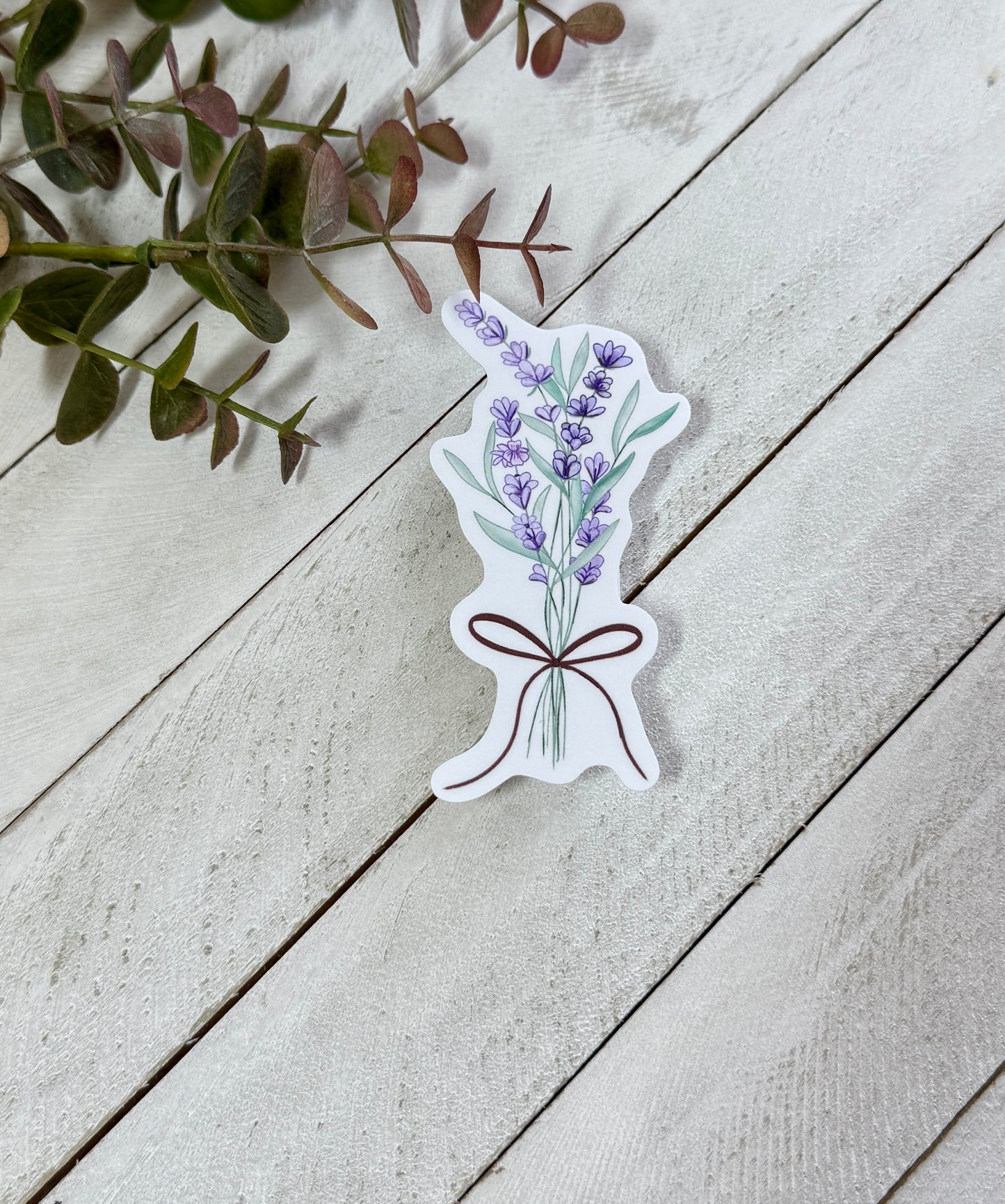 Sticker of a bouquet of lavender on a wooden surface with green leaves.