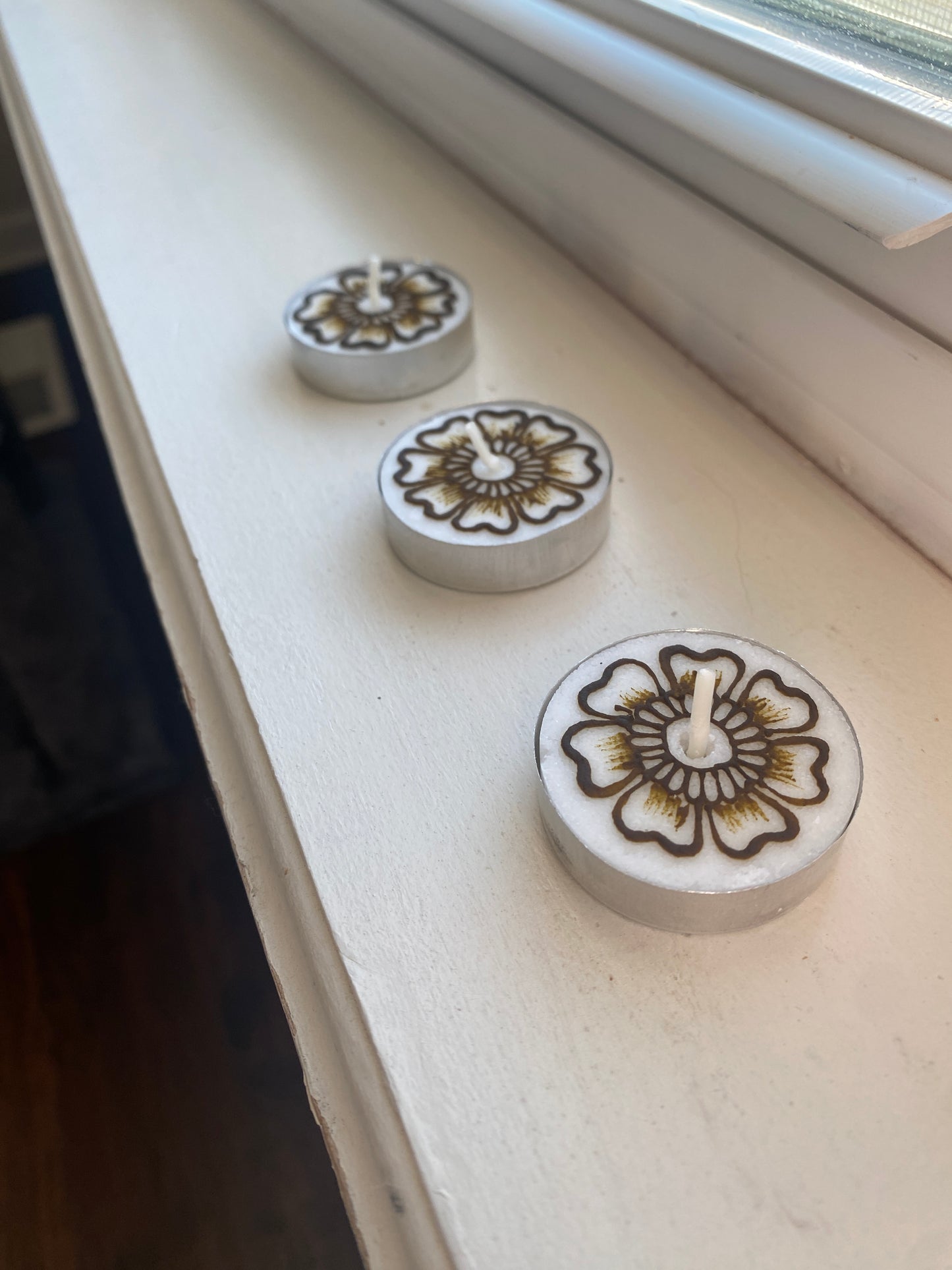 A set of three tea lights with floral designs painted with henna sitting on a white background 