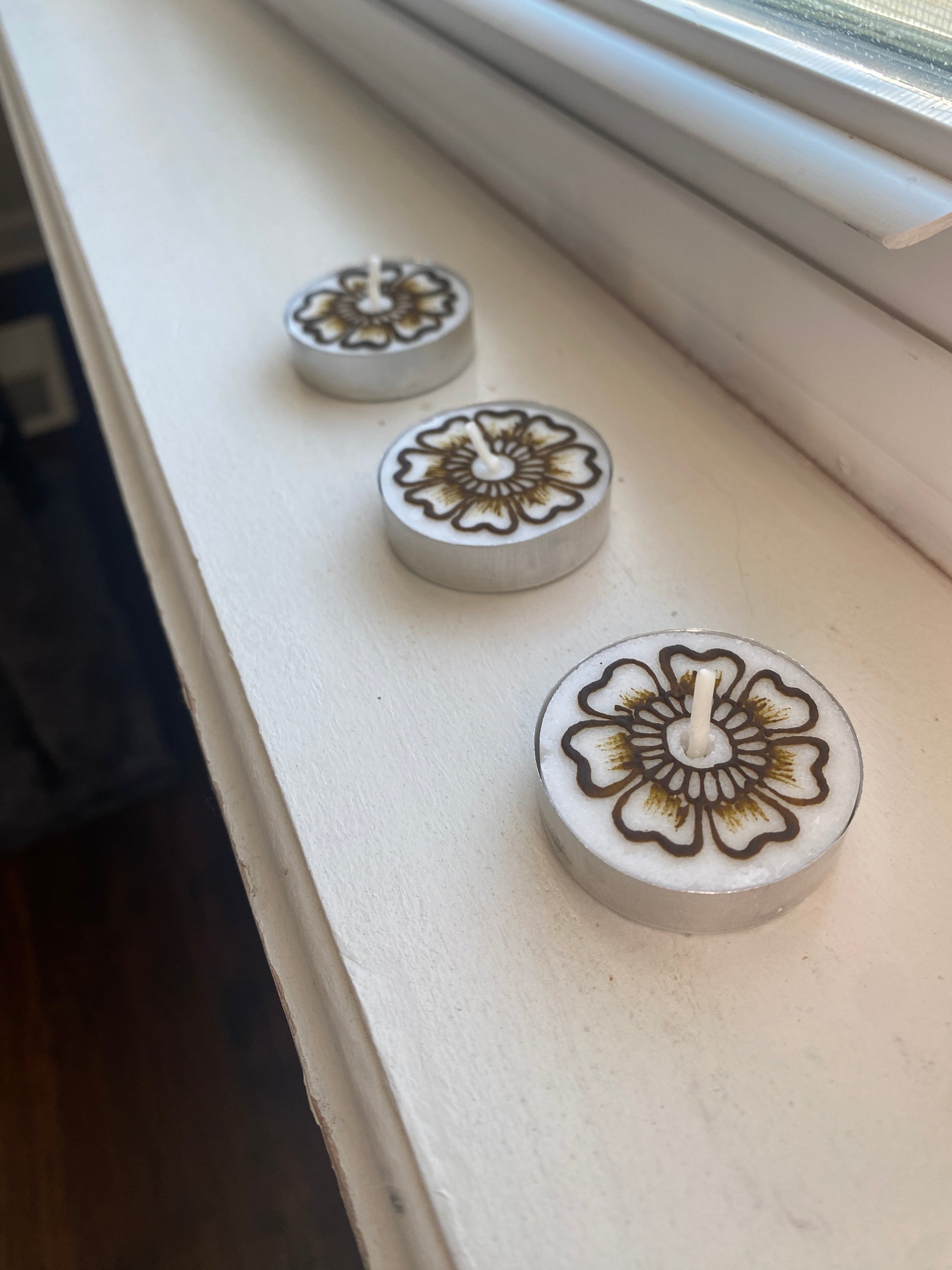 A set of three tea lights with floral designs painted with henna sitting on a white background 