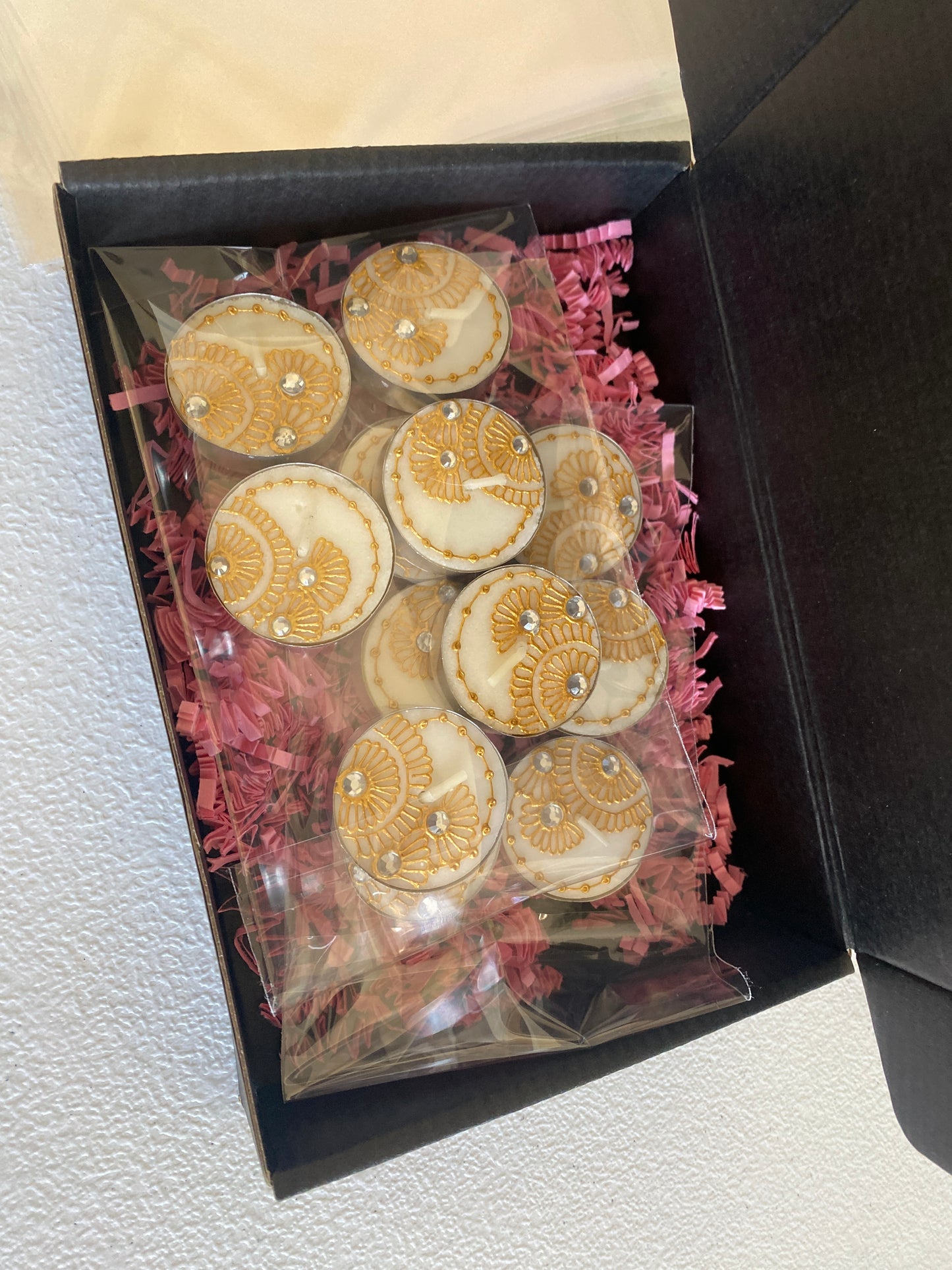 Gold painted tea lights packaged in a black box with pink confetti 