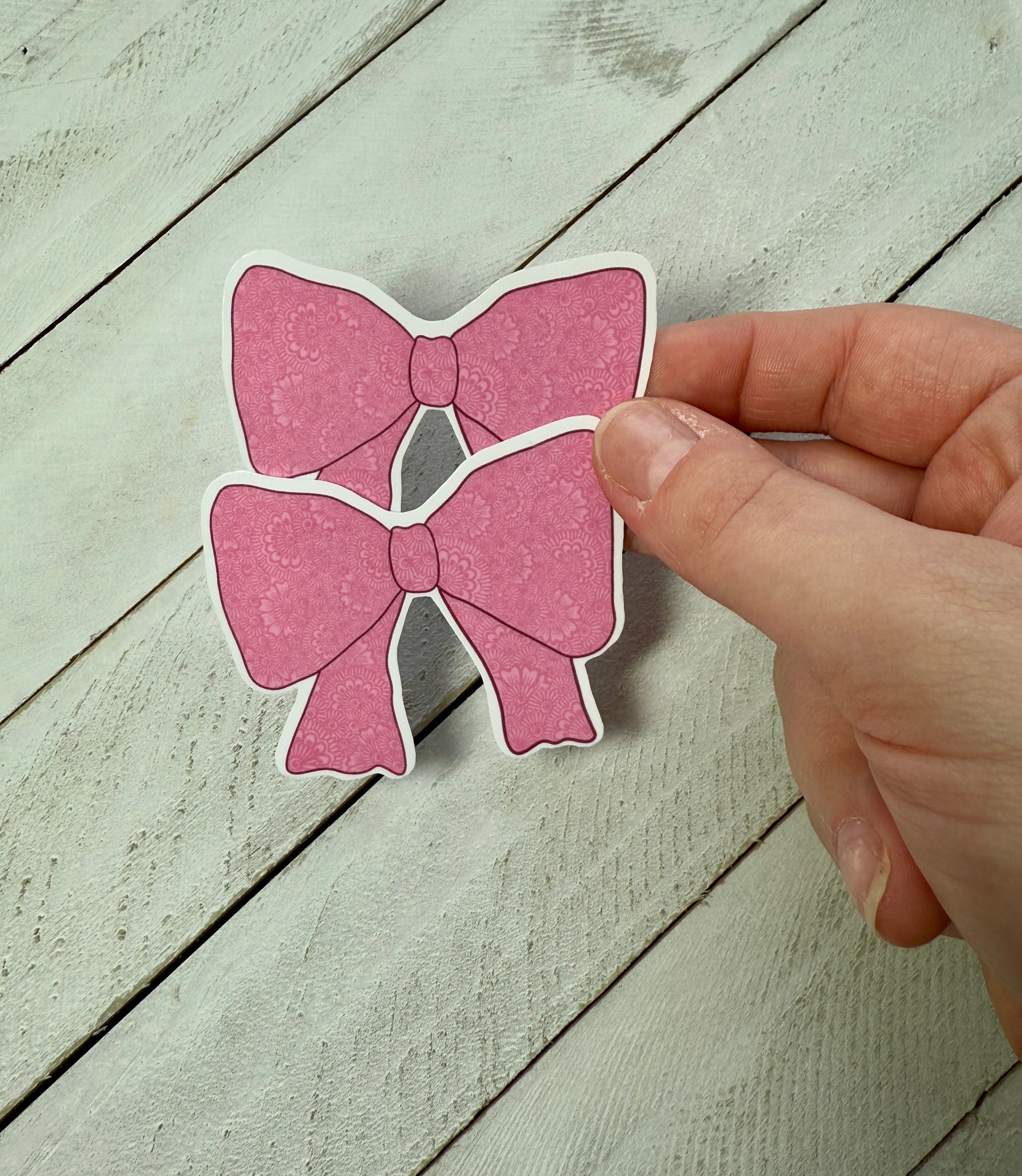 Hand holding a pink bow-shaped sticker on a wooden surface