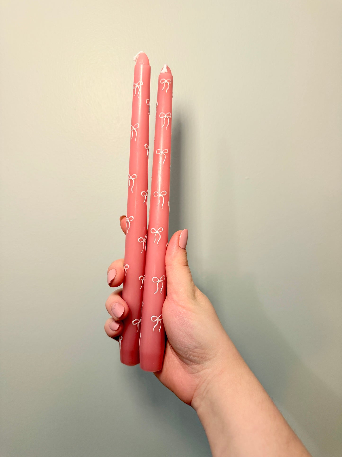Hand holding two pink tapered candles with white patterns against a plain background