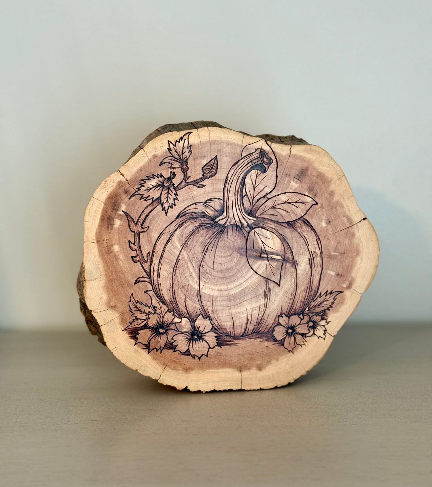 Wooden slice with pumpkin and floral design on a plain background