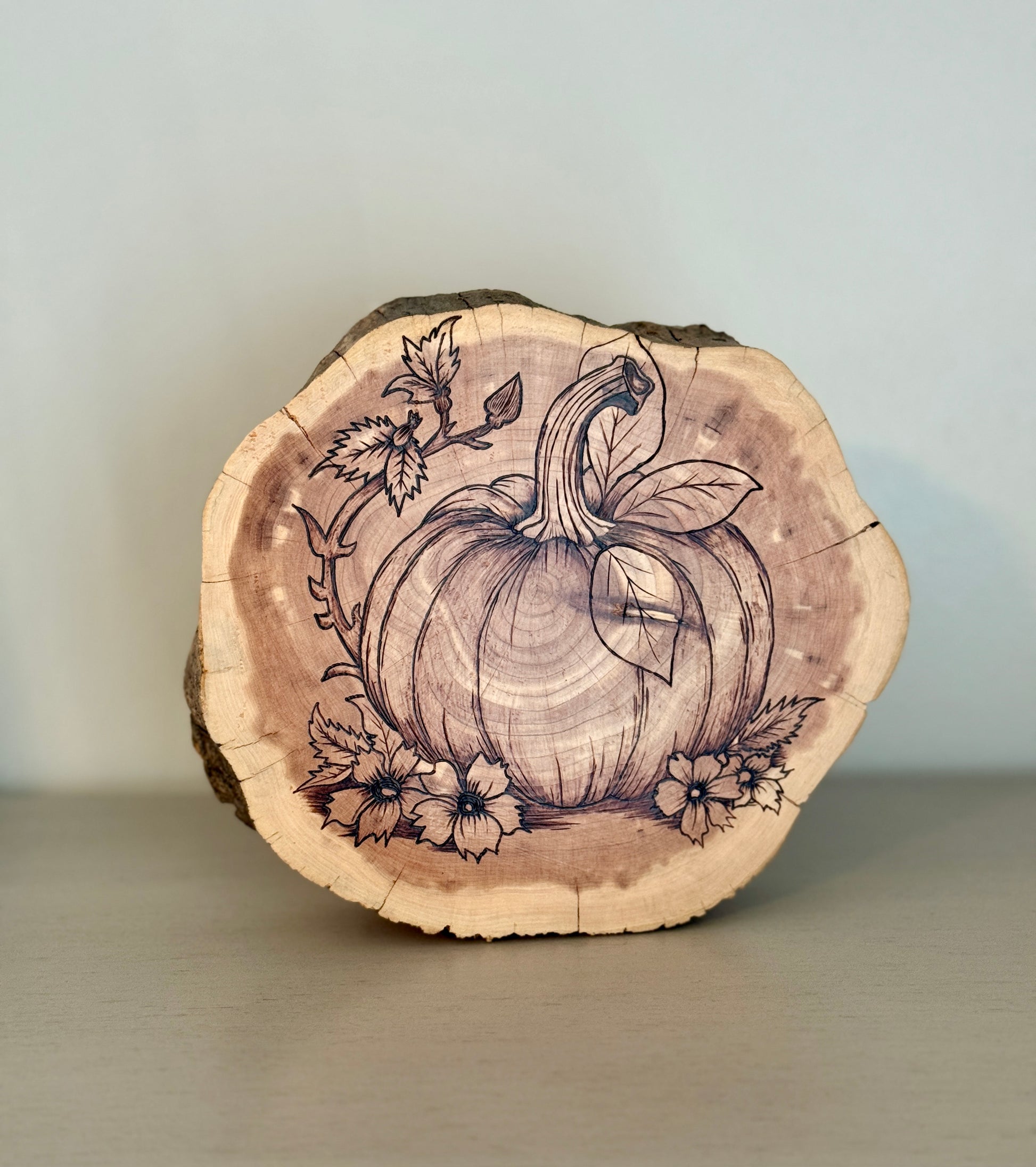 Wooden slice with pumpkin and floral design on a plain background