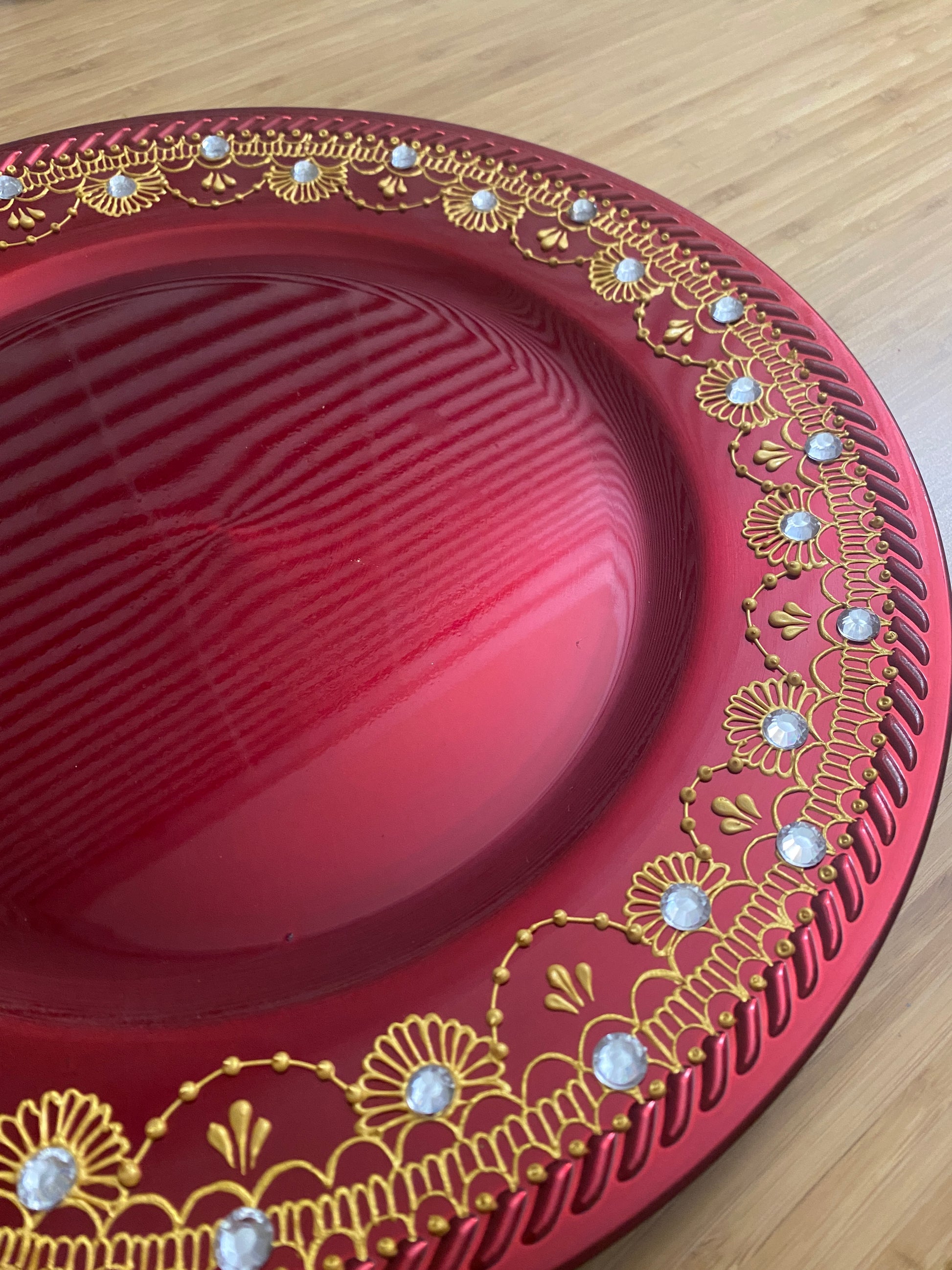 Red circle charger plate with gold painted henna designs and white rhinestones on a wood background