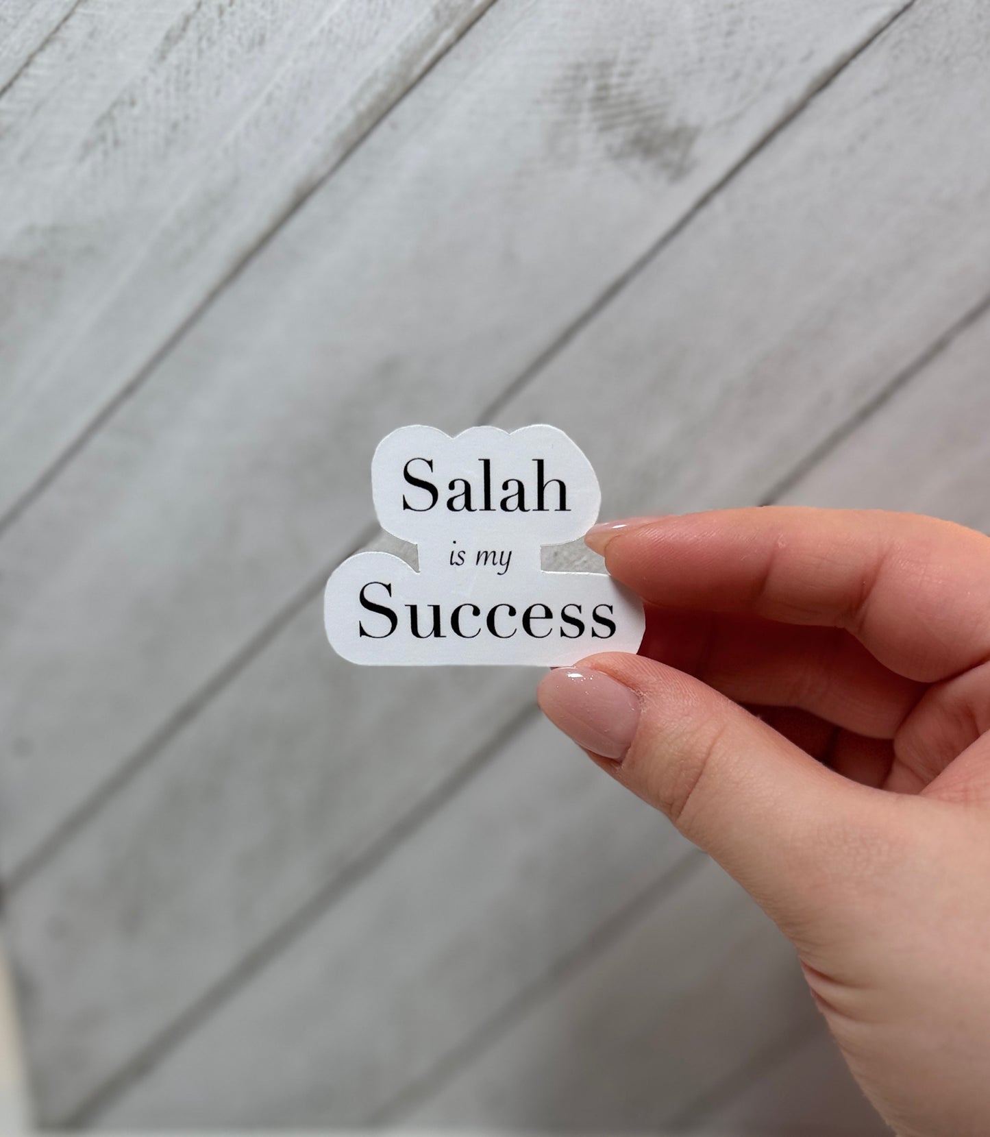 Hand holding a sticker with 'Salah is my Success' text against a wooden background