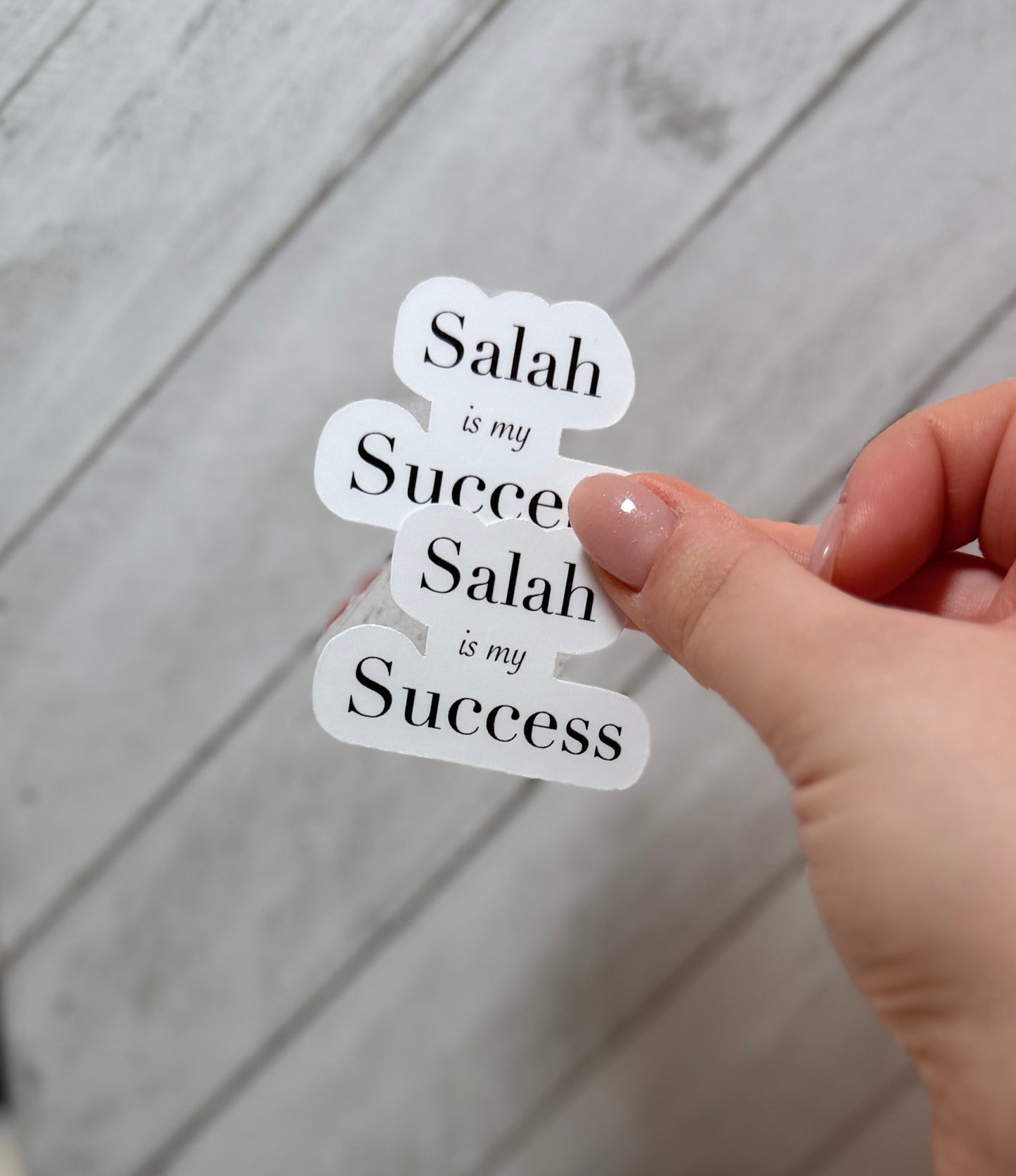 Hand holding a sticker with 'Salah is my Success' text on a wooden surface