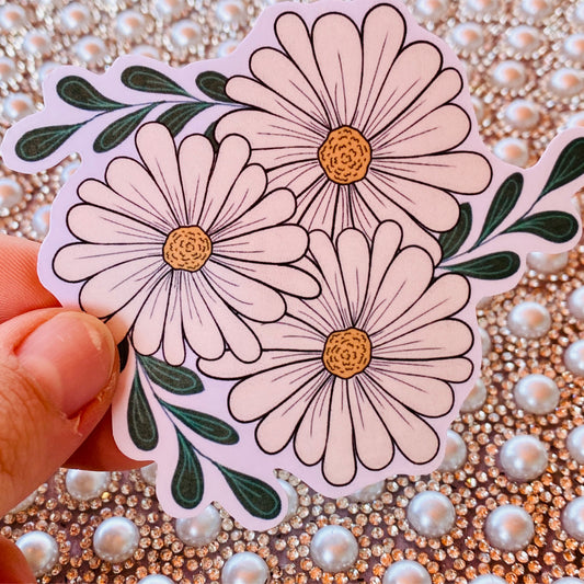 A hand holding a sticker with three daisy flowers against a sparkle background