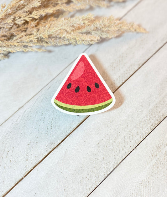 Watermelon slice sticker on a wooden surface with dried plants in the background