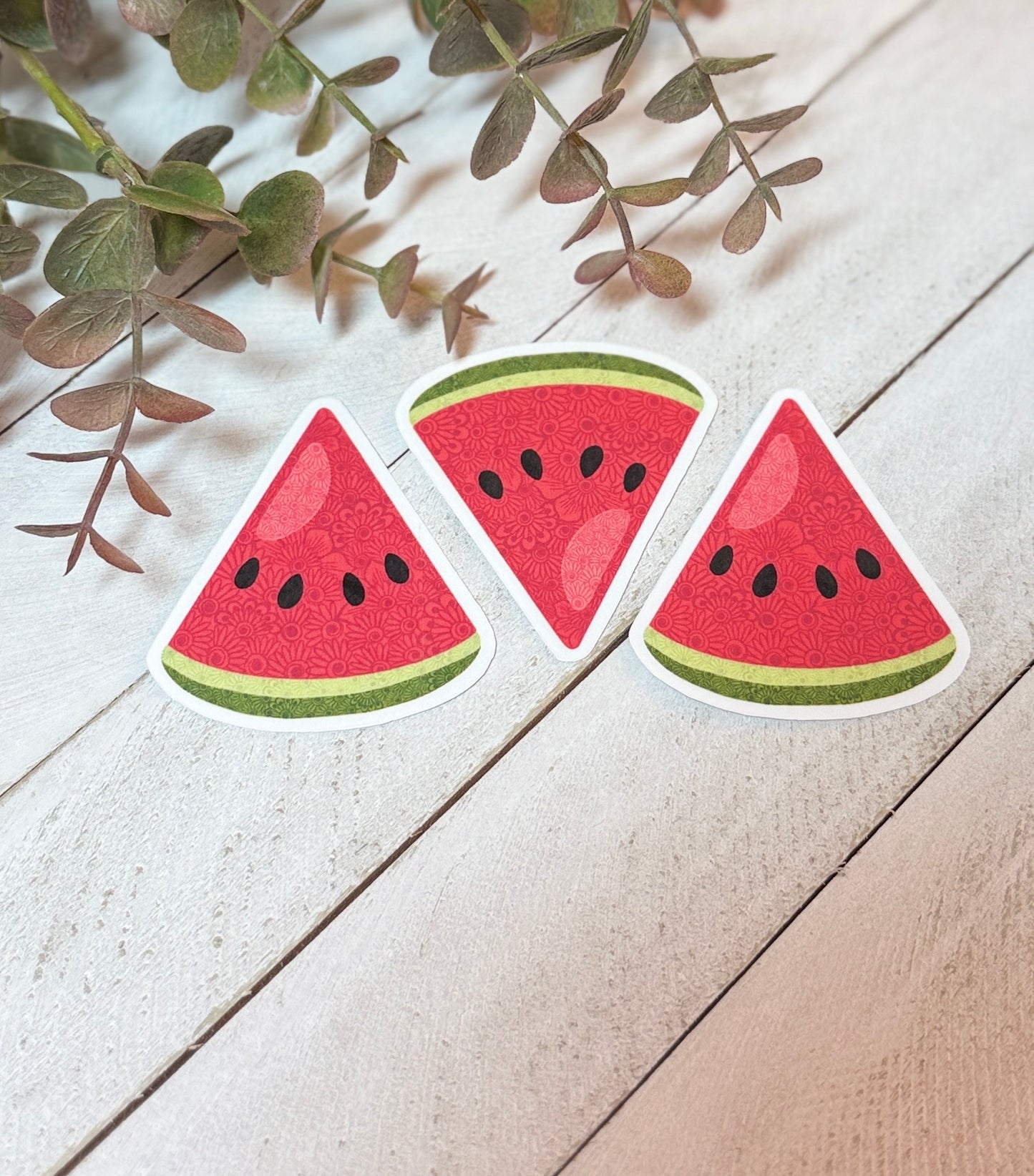 Three watermelon slice stickers on a wooden surface with green leaves.
