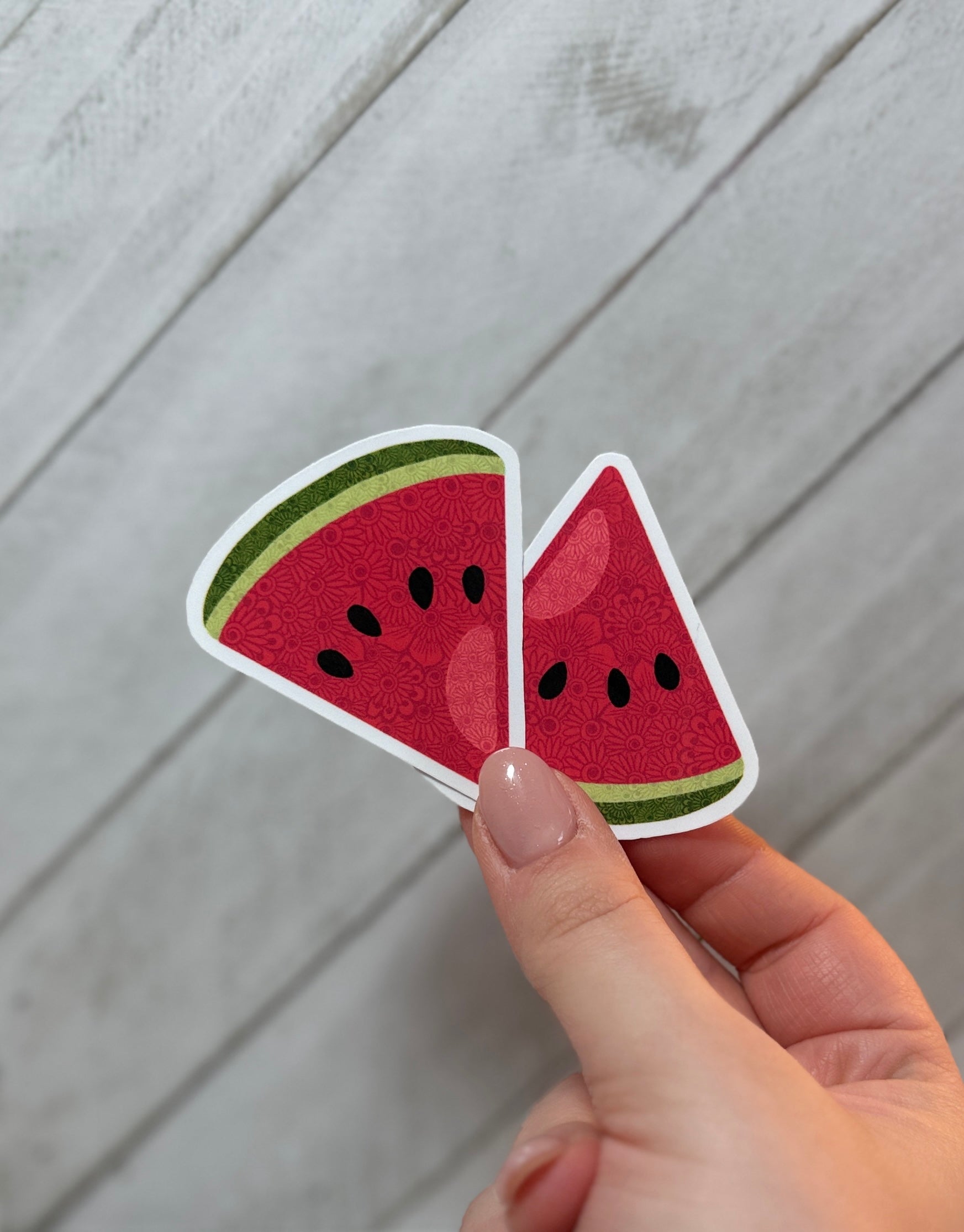 Two watermelon slice stickers held between fingers against a wooden background