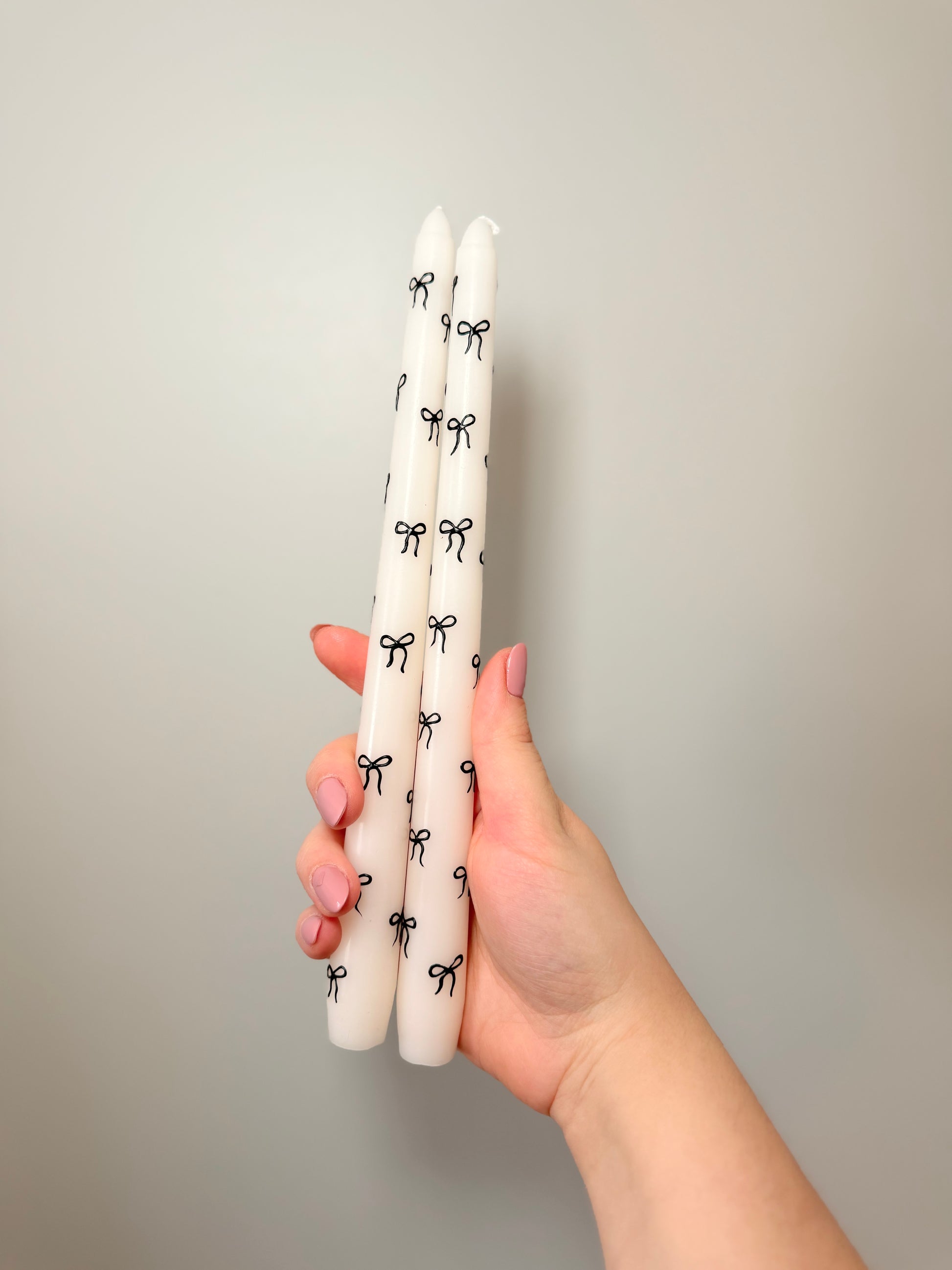 Hand holding three white candles with black bow designs against a plain background