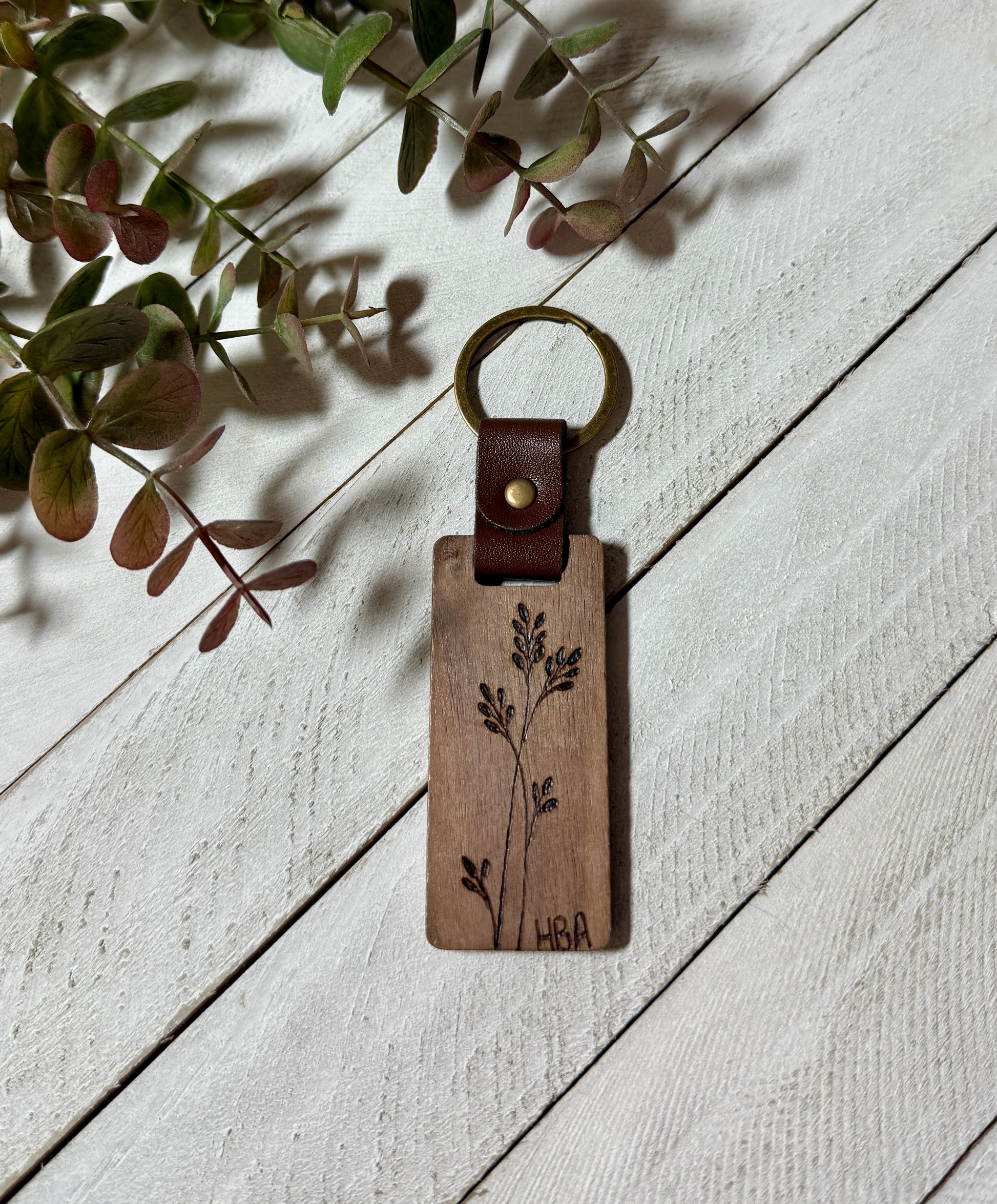 Wooden keychain with engraved design on a light wooden surface with leaves.