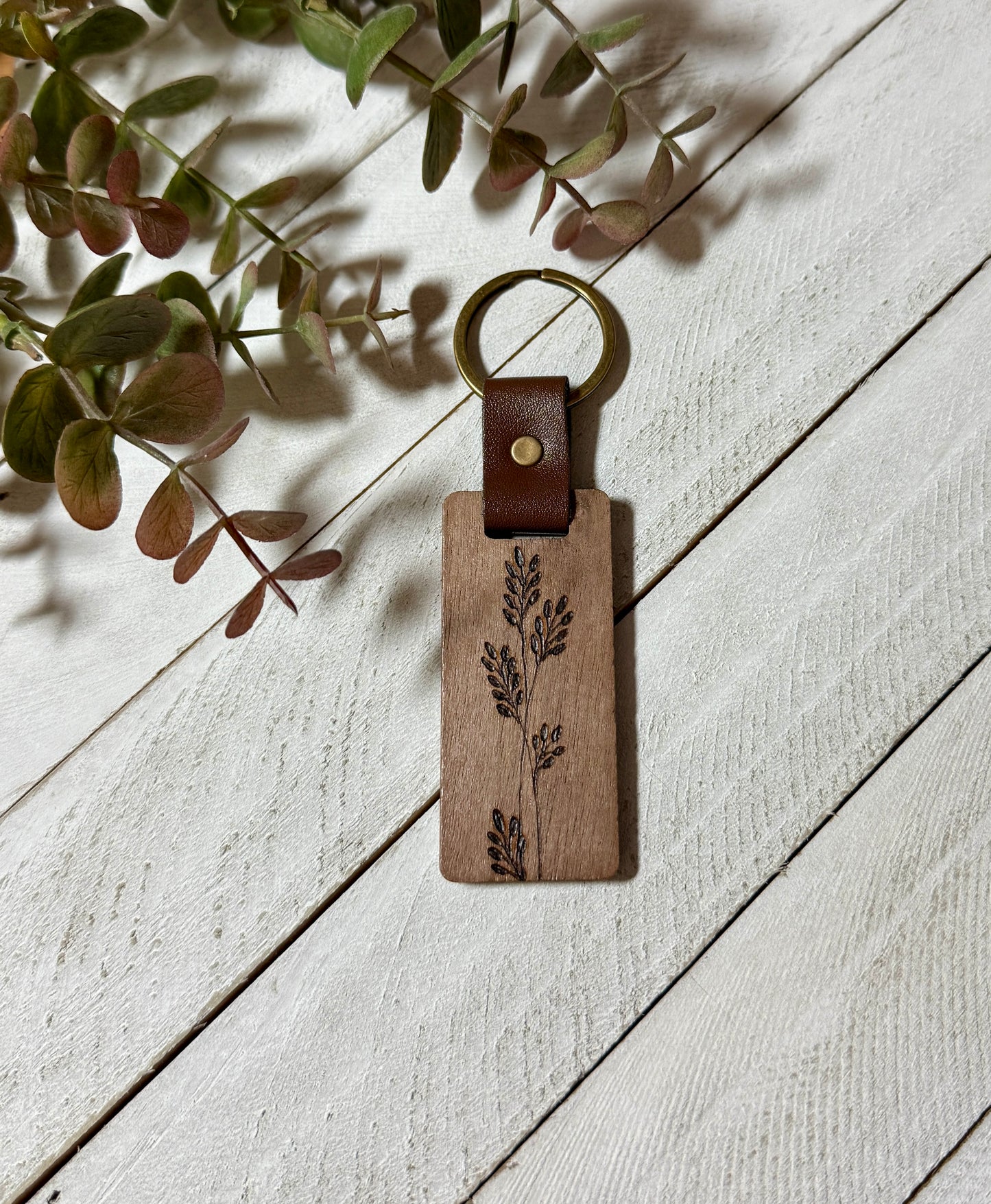 Wooden keychain with leather accent on a light wooden surface with greenery.