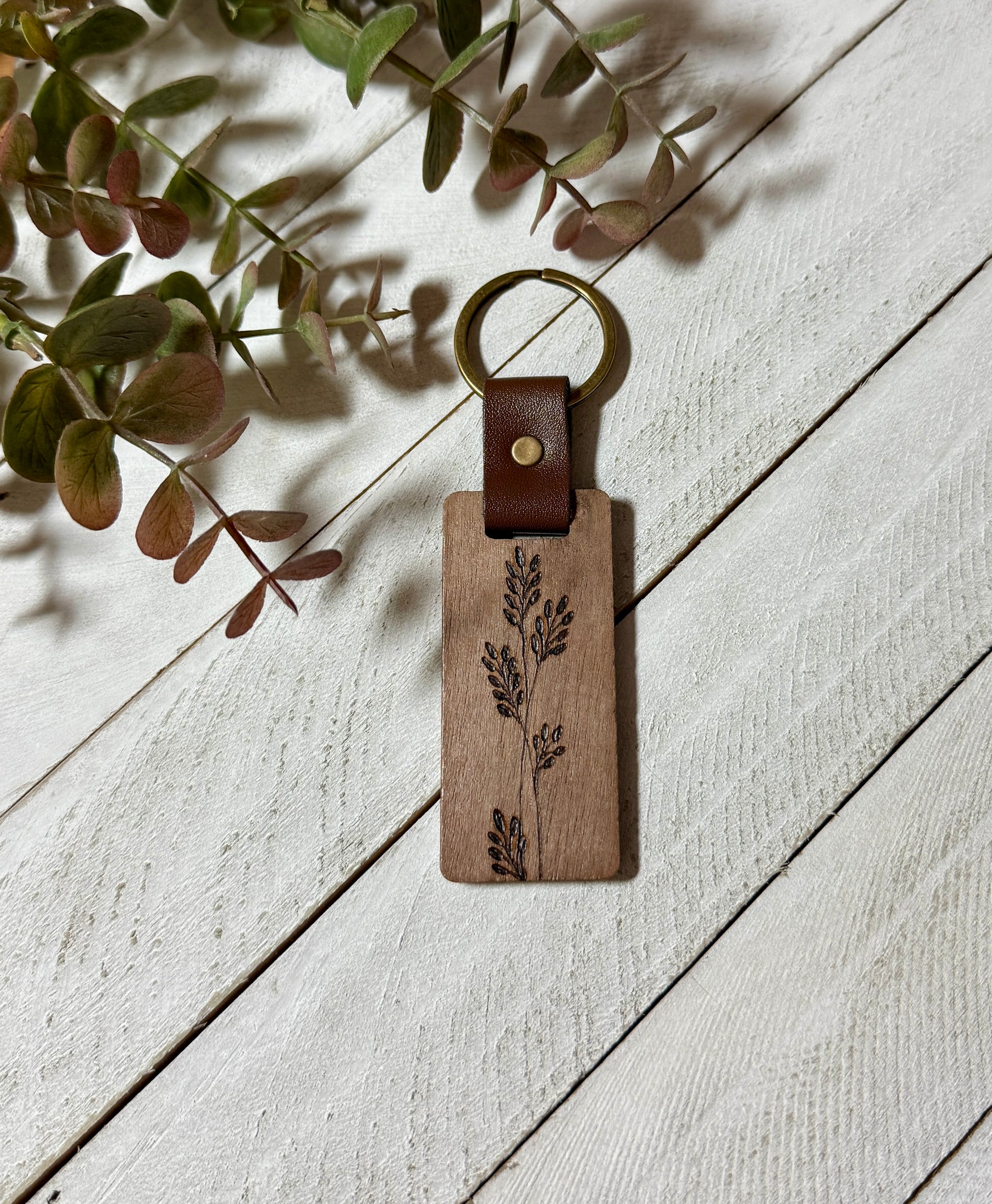 Wooden keychain with leather accent on a light wooden surface with greenery.