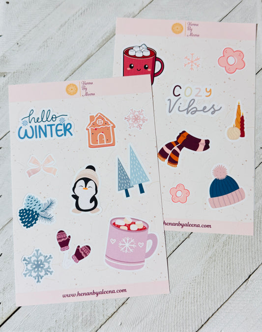 Two sheets of winter-themed stickers with cute illustrations on a wooden surface.