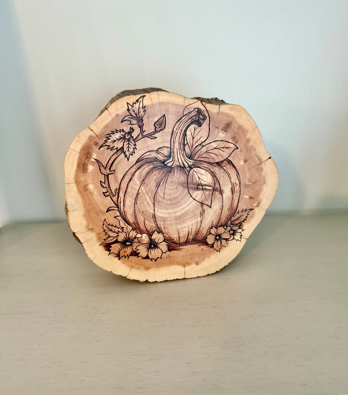 Wooden slice with pumpkin and floral design on a plain background