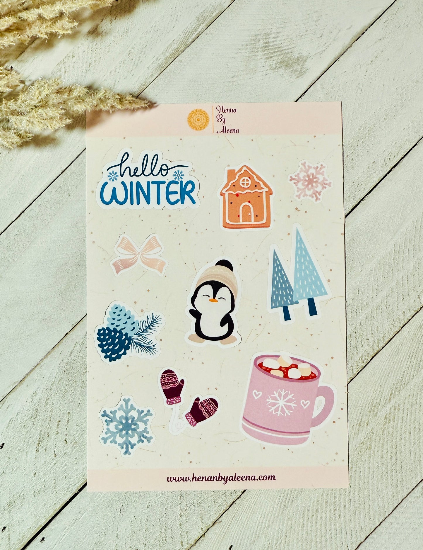 Sheet of winter-themed stickers with 'hello winter' text, penguin, hot chocolate, and other elements on a wooden surface.