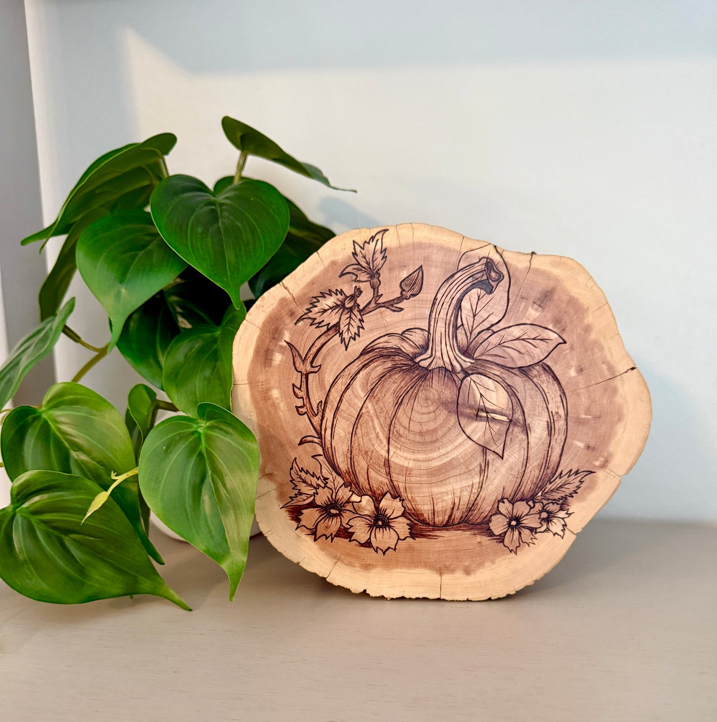 Wooden coaster with pumpkin design next to a green plant